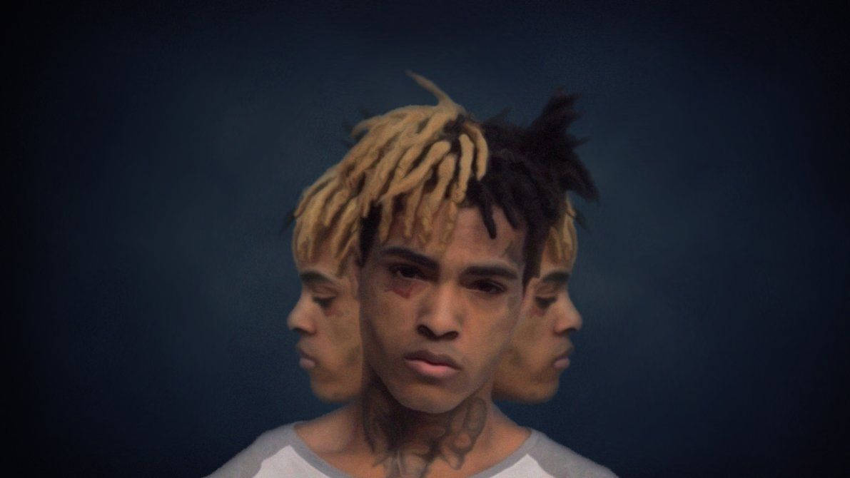 XXXTENTACION 桌布 壁紙 — 一個年輕男子，金色和黑色辮子，在深藍色背景上，有兩個幽靈般的側面輪廓，凝視著。