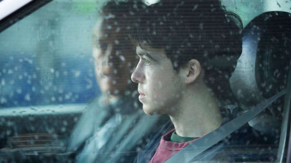 演員 桌布 壁紙 — 一個年輕男子凝視著佈滿雨點的車窗外，神情沉思，另一個人坐在他旁邊。