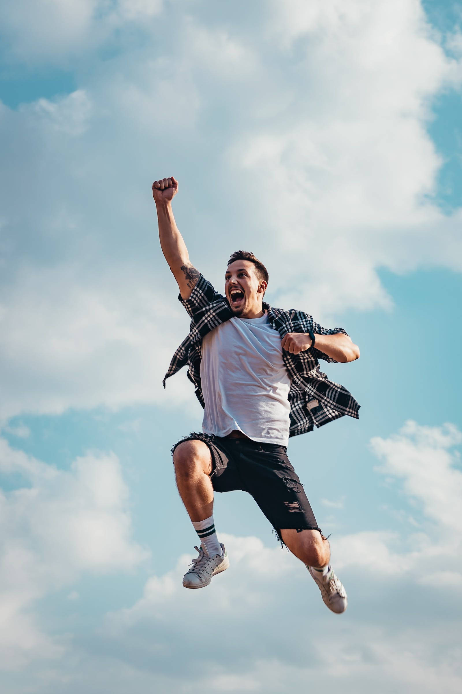 Jumping 桌布 壁紙 — 一個年輕男子在明亮的藍天和白雲下，高舉拳頭，歡欣跳躍，展現勝利姿態。