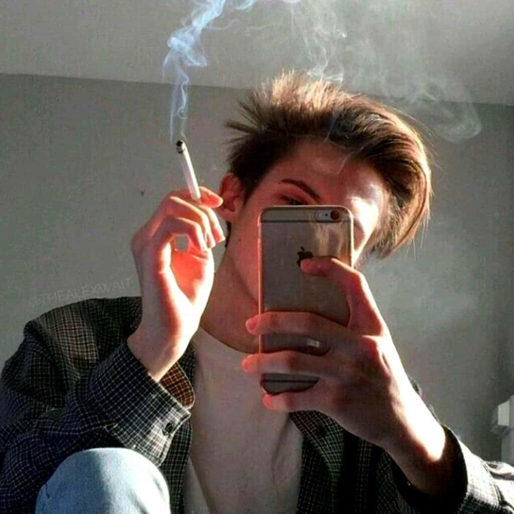 selfie 桌布 壁紙 — 一個年輕男子在昏暗的房間裡用智慧型手機對著鏡子自拍，同時吸煙。