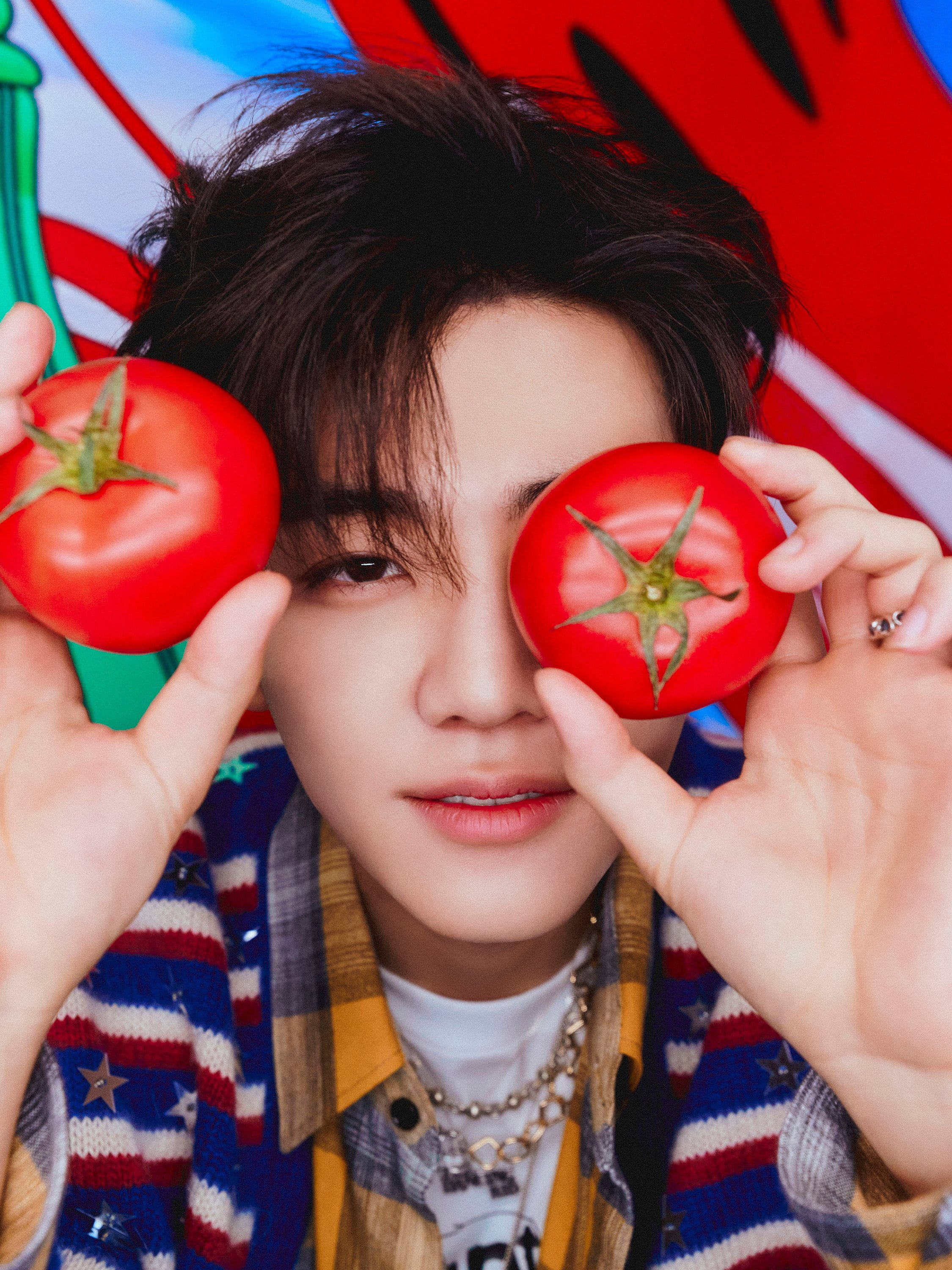 jaemin 桌布 壁紙 — 一個年輕男子在色彩繽紛的抽象背景前，頑皮地將兩個鮮紅番茄舉在眼前。