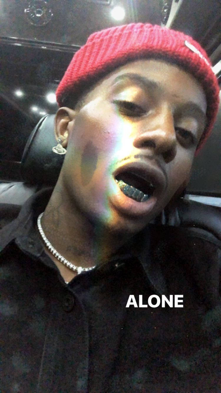 Carti 桌布 壁紙 — 一個年輕男子戴著紅色毛帽和黑色襯衫坐在車裡，彩虹光反射在他的臉和格柵上。