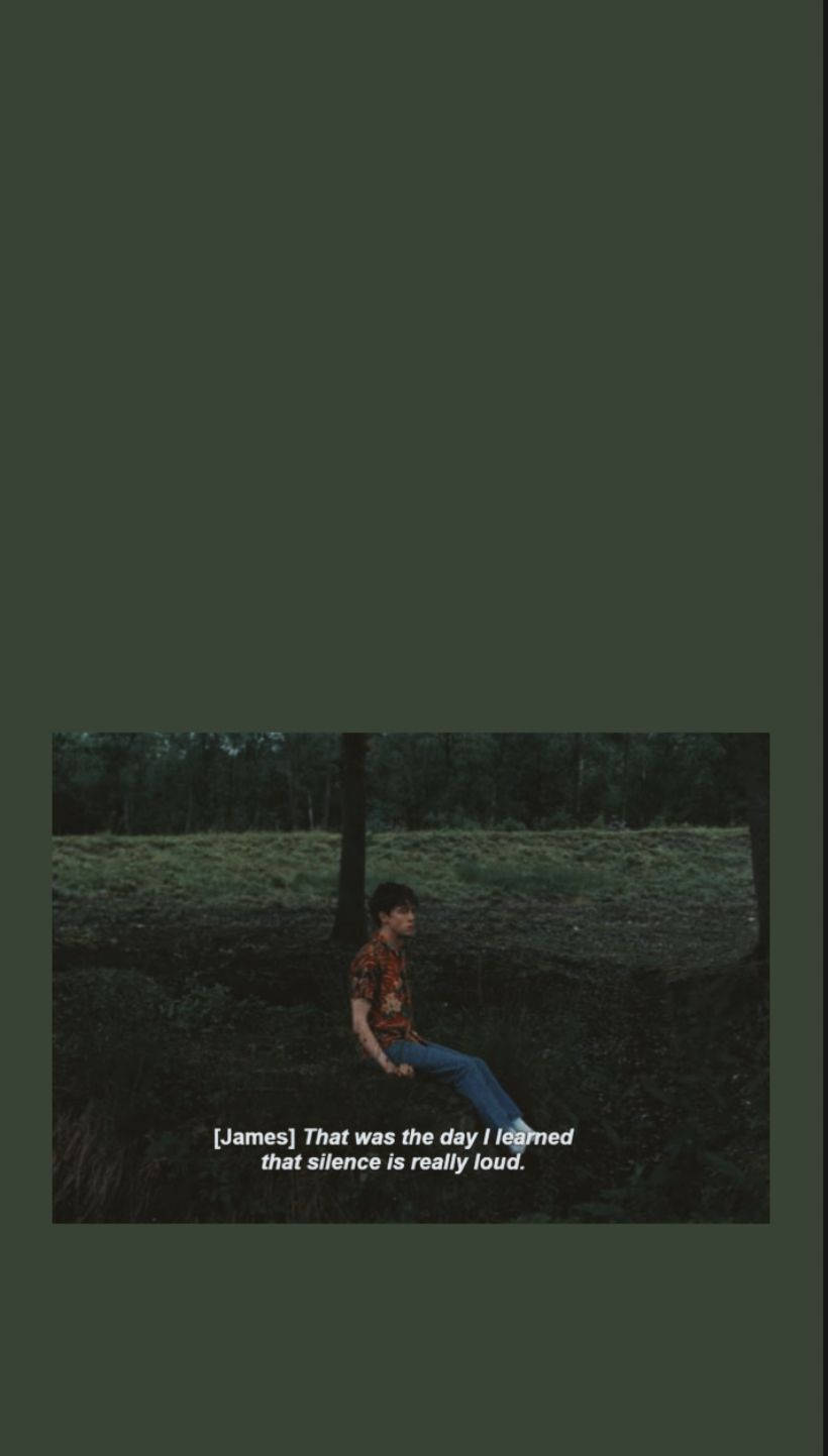 油漬搖滾 桌布 壁紙 — 一個年輕男子獨自坐在昏暗的森林空地中，穿著圖案襯衫和牛仔褲，被高大的樹木和柔軟的苔蘚包圍，在柔和的綠色光線下。