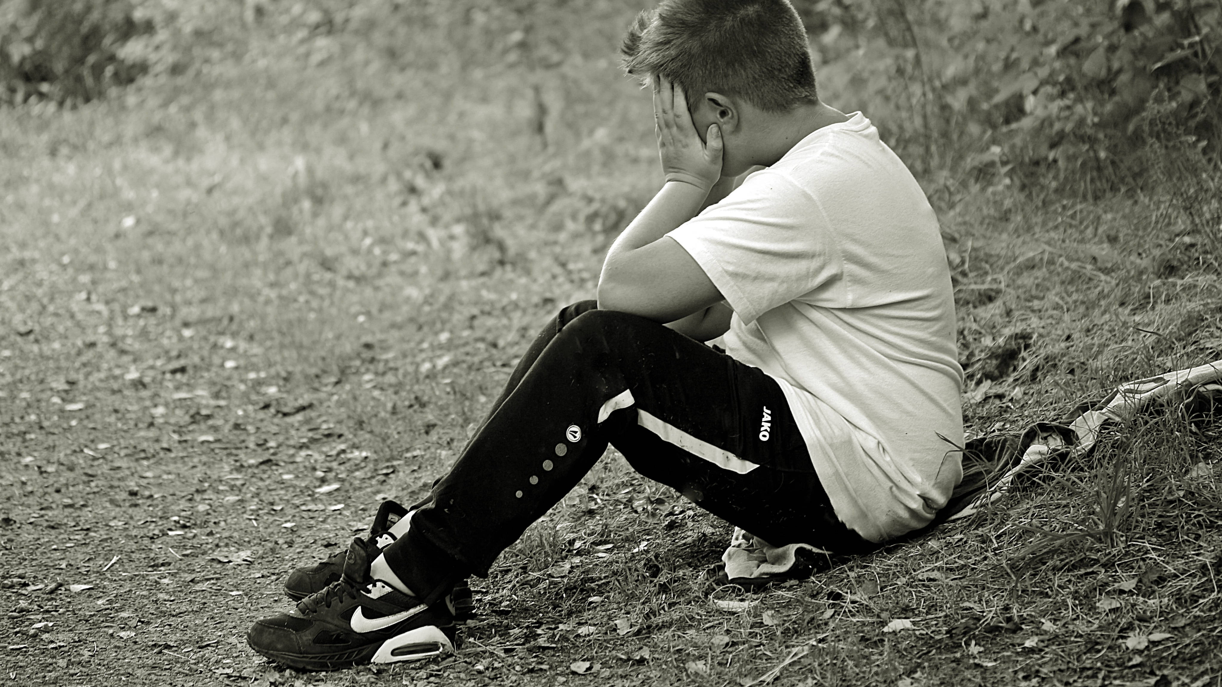 crying sad boy 桌布 壁紙 — 一個年輕男子獨自坐在草地上，雙手掩面，黑白照片。