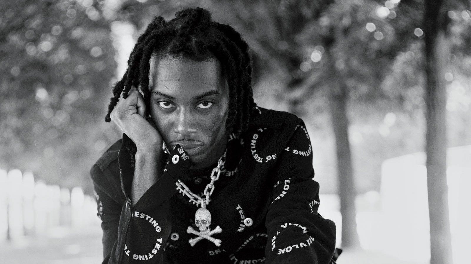 Carti 桌布 壁紙 — 一個年輕男子留著辮子，在戶外用手托著頭的黑白肖像。