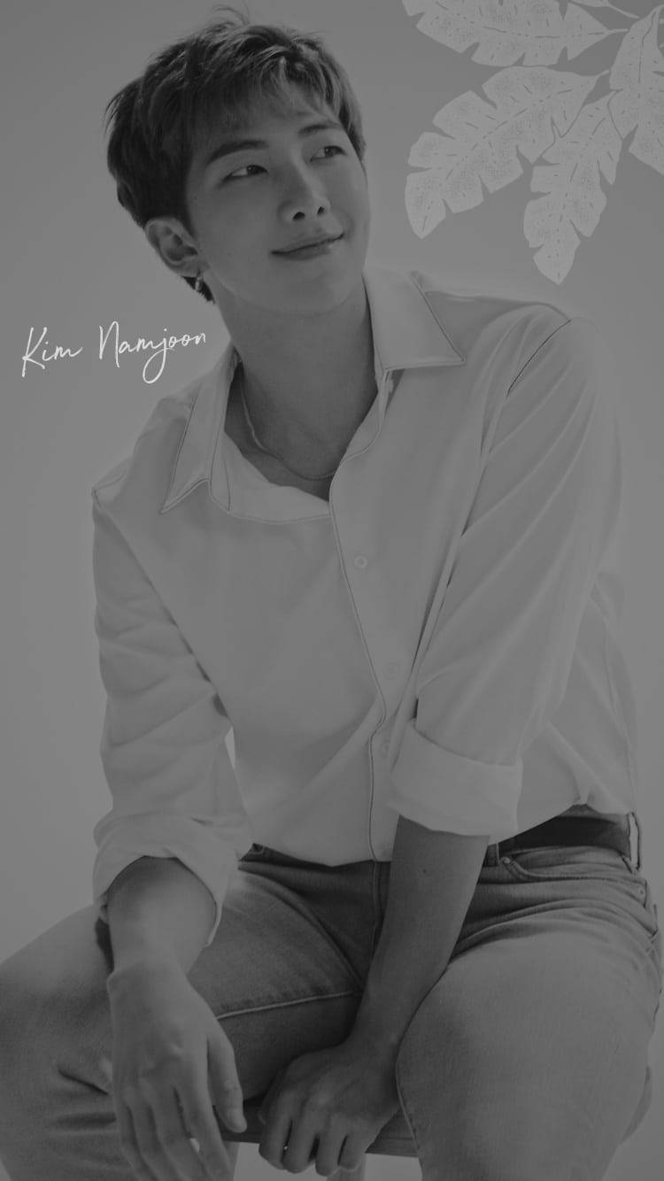 Rm 桌布 壁紙 — 一個年輕男子穿著白襯衫和牛仔褲，在帶有葉子剪影的極簡背景前微笑坐著的單色肖像。
