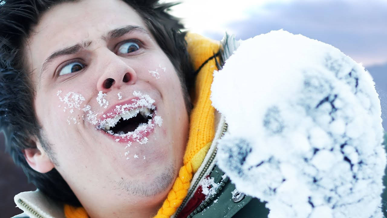 Snowing 桌布 壁紙 — 一個年輕男子臉上沾滿雪，笑著拿著雪球，冬日場景。