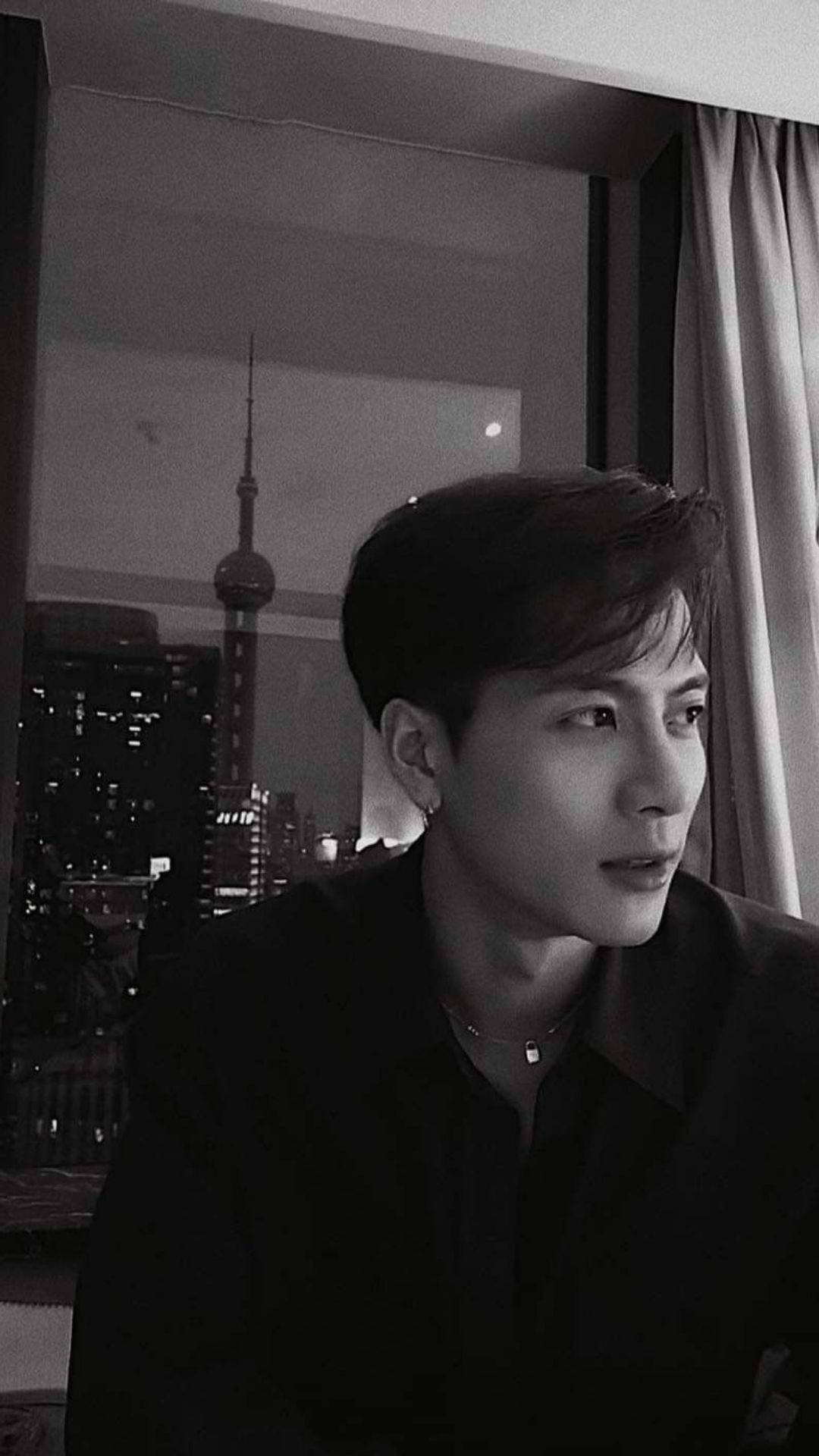 王嘉爾 桌布 壁紙 — 一個年輕男子若有所思地望向窗外，欣賞夜晚燈火璀璨的上海天際線。