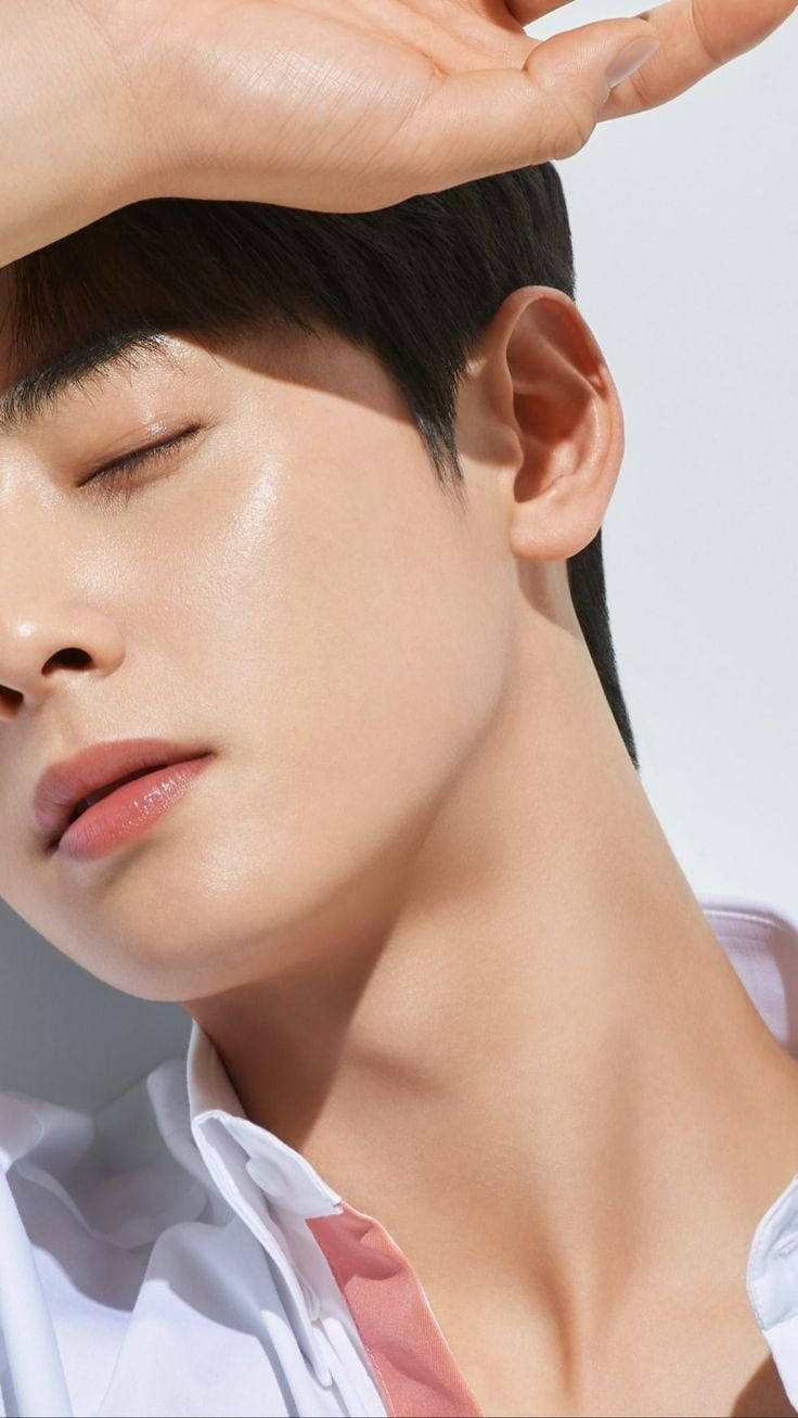 Eunwoo 桌布 壁紙 — 一個年輕男子閉上眼睛，用手遮擋臉部免受強烈陽光照射，身穿帶有粉紅色點綴的白色襯衫。