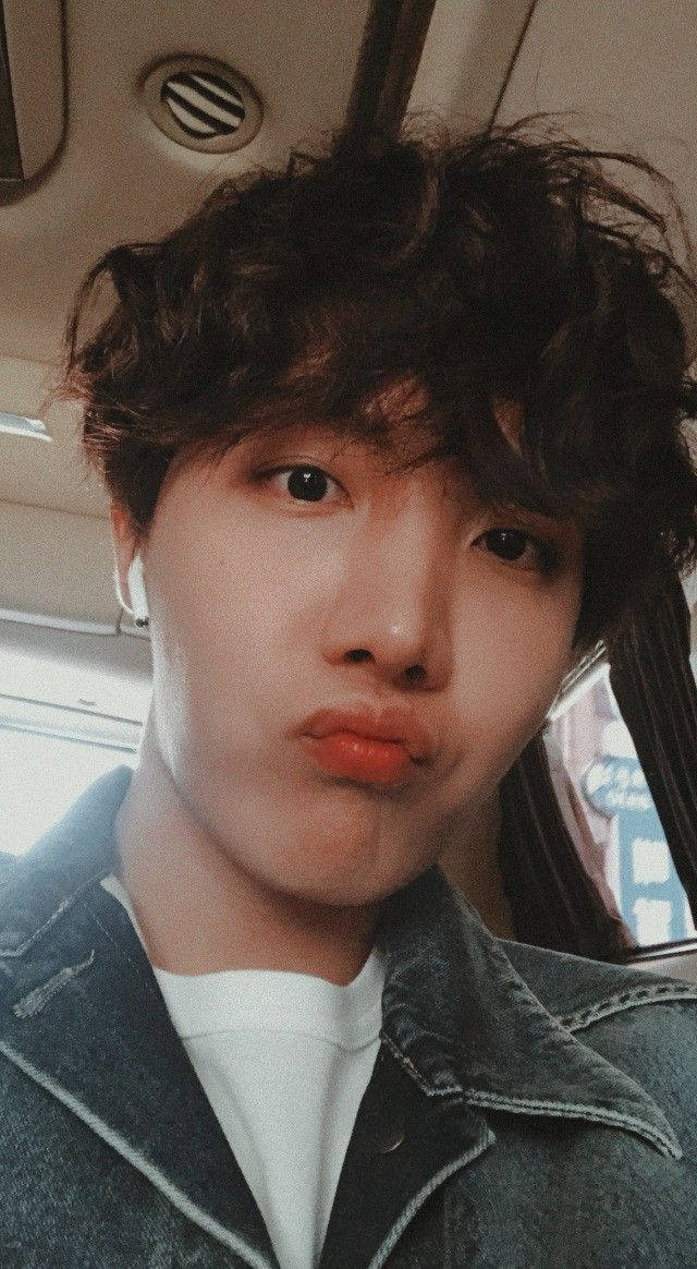 j-hope 桌布 壁紙 — 一個年輕男子頭髮凌亂，穿著牛仔外套在車內做出俏皮的嘟嘴表情。