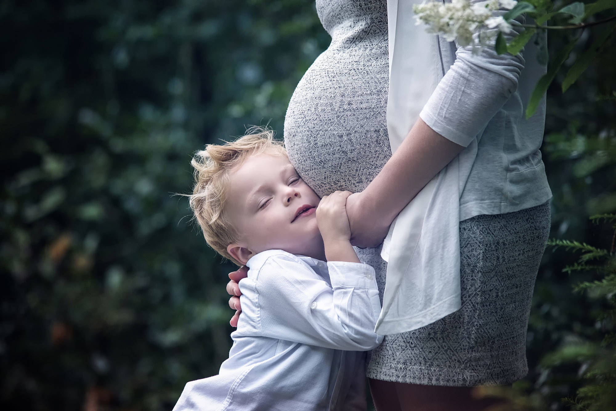 Pregnant 桌布 壁紙 — 一個年輕男孩閉著眼睛，在茂密的綠色森林中安詳地靠在母親懷孕的肚子上休息。