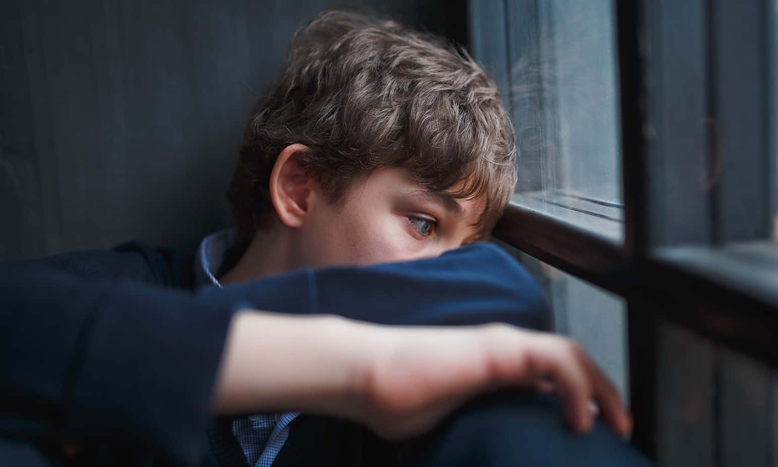 Depressed 桌布 壁紙 — 一個年輕男孩頭髮凌亂，在昏暗的房間裡把頭靠在手臂上，凝視著窗外。