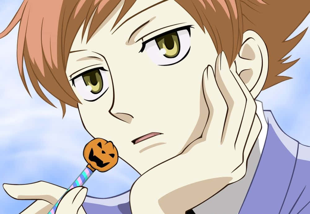 Kaoru Hitachiin 桌布 壁紙 — 一個年輕的動漫男孩，棕色頭髮和綠色眼睛，拿著南瓜棒棒糖，臉頰靠在手上，背景是明亮的藍天。