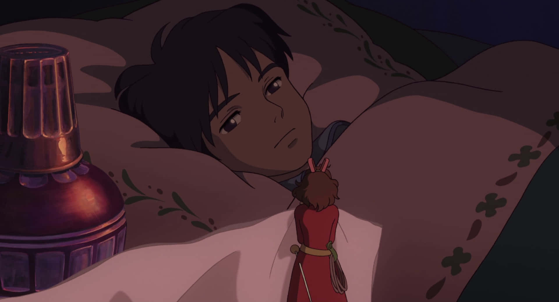 The Secret World Of Arrietty 桌布 壁紙 — 一個年輕的動漫角色躺在有圖案的毯子下的床上，在昏暗的燈光下拿著一個小紅色娃娃，旁邊有一盞發光的燈。