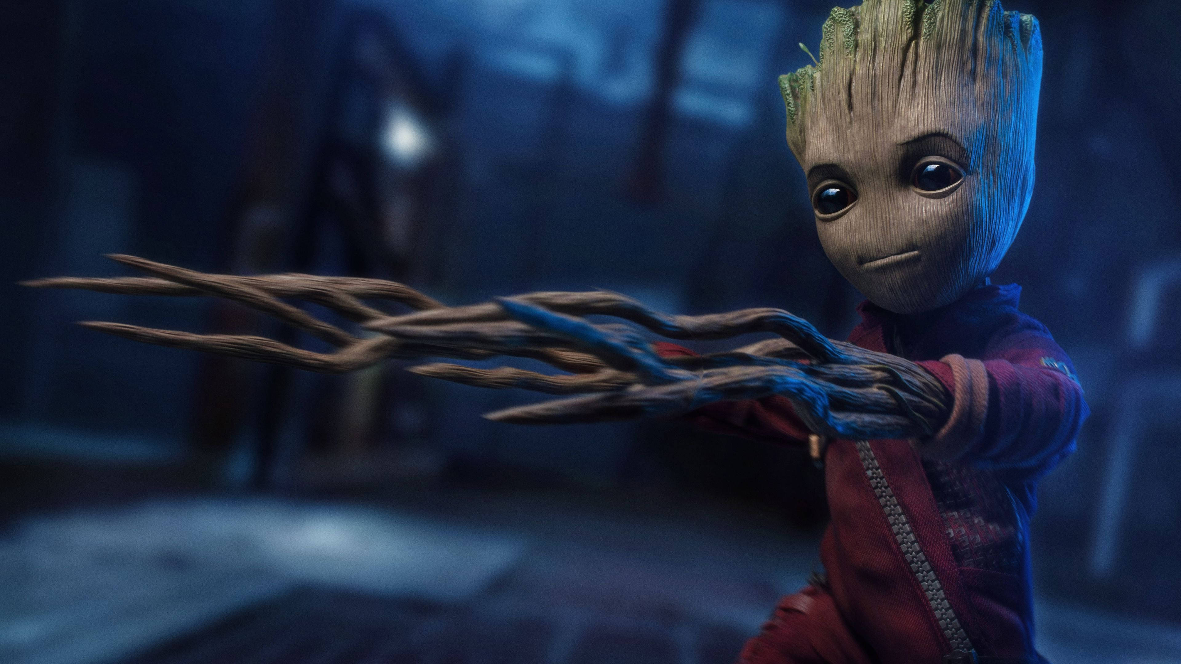 4K Guardians Of The Galaxy 桌布 壁紙 — 一個年輕的樹狀角色，有著樹枝般的手臂，在昏暗、憂鬱的藍色環境中伸出手。