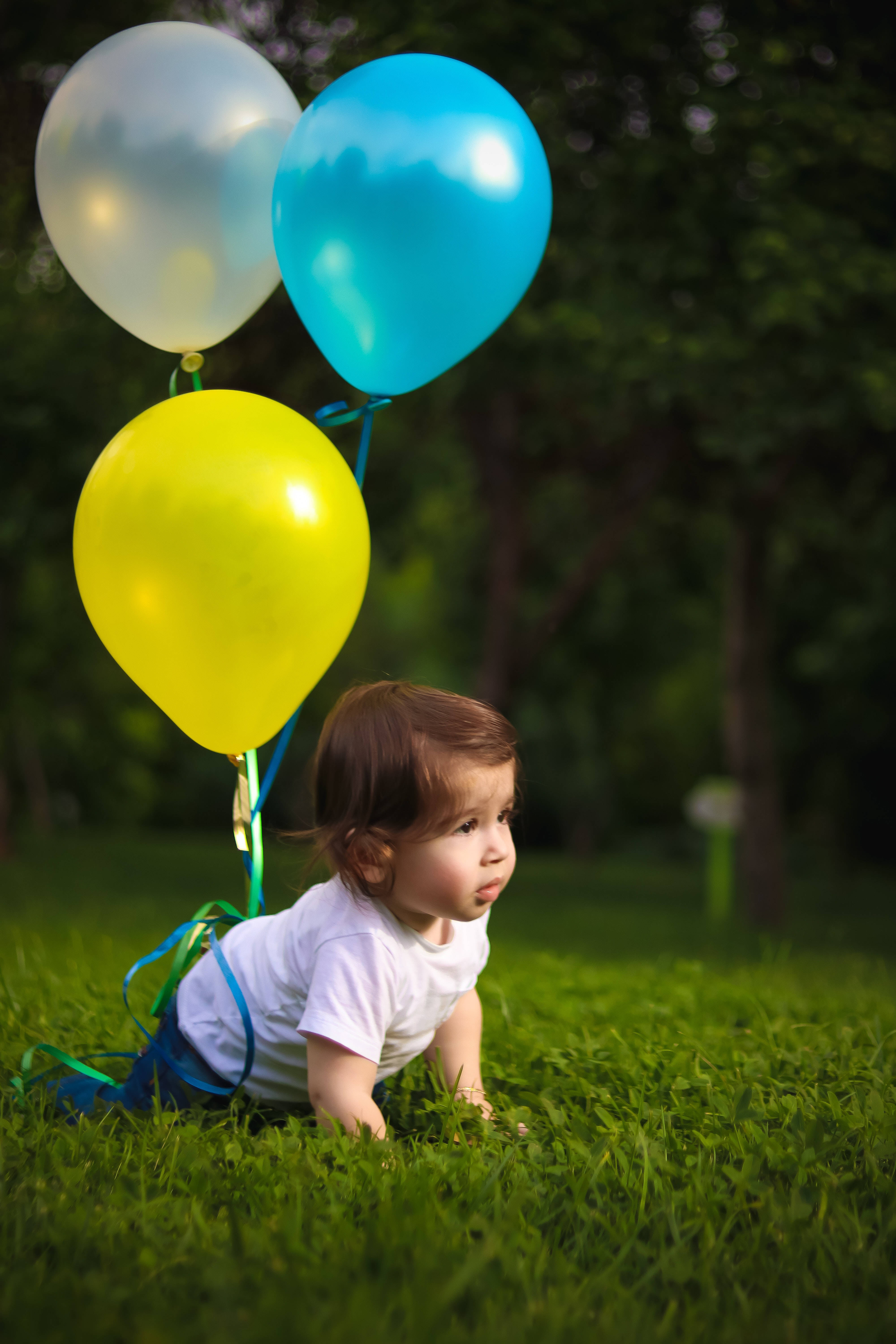 Baby Boy 桌布 壁紙 — 一個幼兒在茂密的綠色草地上爬行，手持三個色彩繽紛的氣球，背景是柔和模糊的森林。