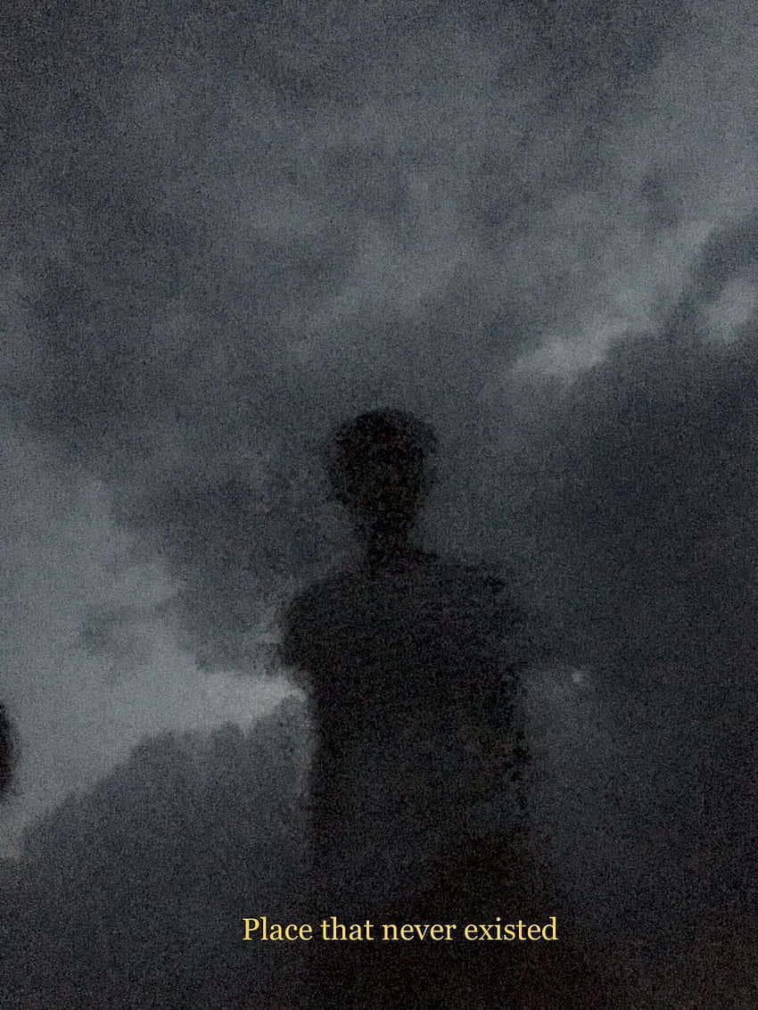 Silhouette 桌布 壁紙 — 一個幽靈般的人形剪影，站在帶有微弱雲層和顆粒感電影效果的紋理深灰色天空前。
