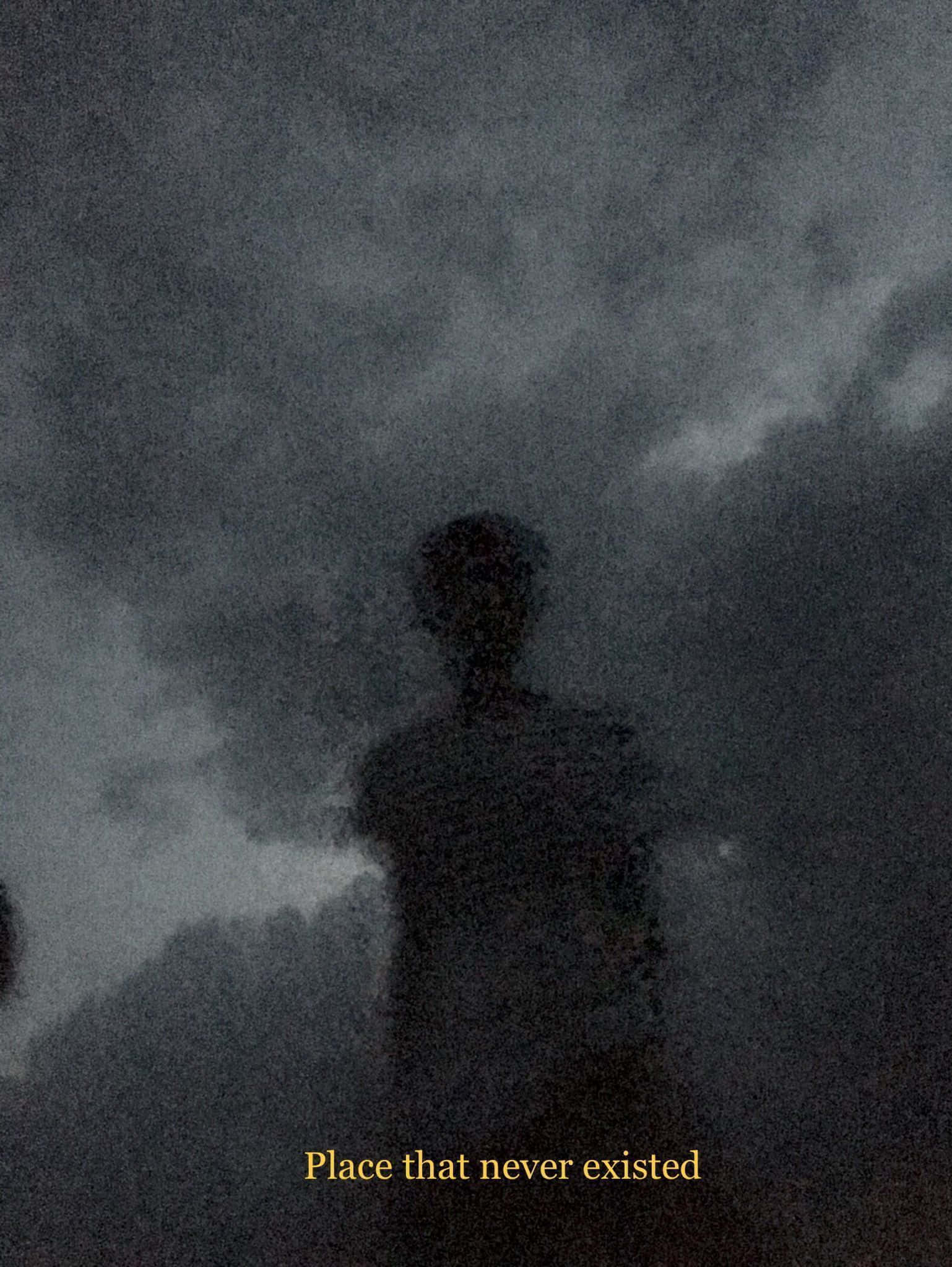 桌布 壁紙 — 一個幽靈般的人形剪影站在旋轉的深灰色天空前，底部有微弱的金色文字。
