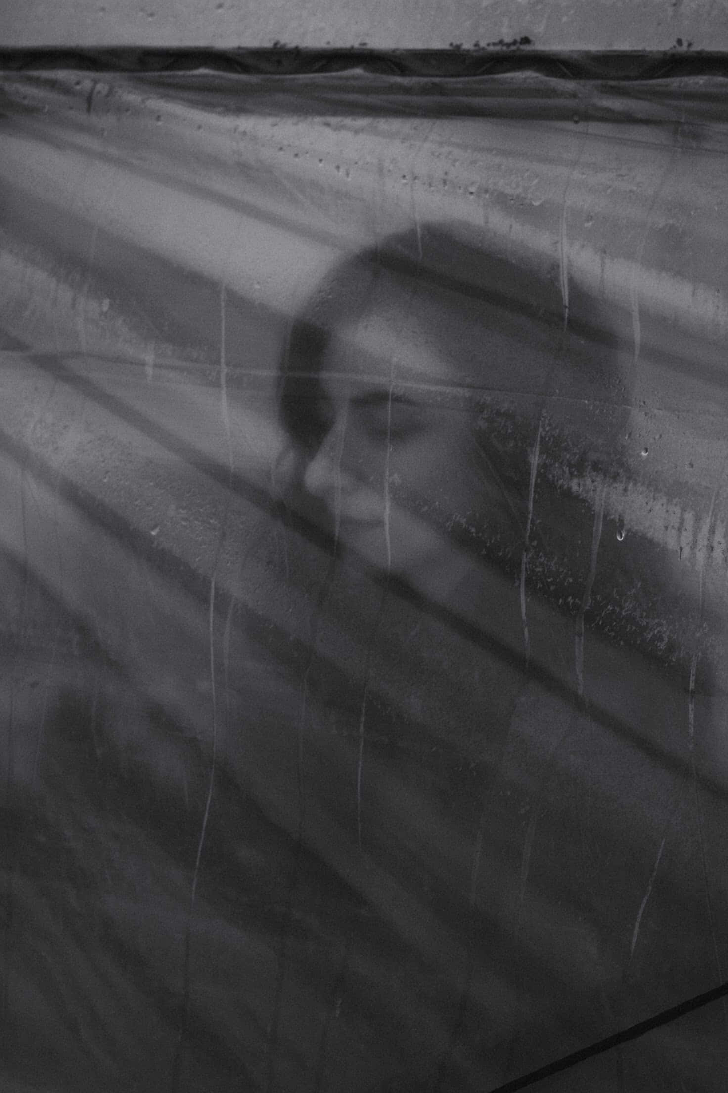 Sad Vibes 桌布 壁紙 — 一個幽靈般的黑白肖像，女人的臉在雨水斑駁的玻璃後模糊，伴隨著柔和的光線。
