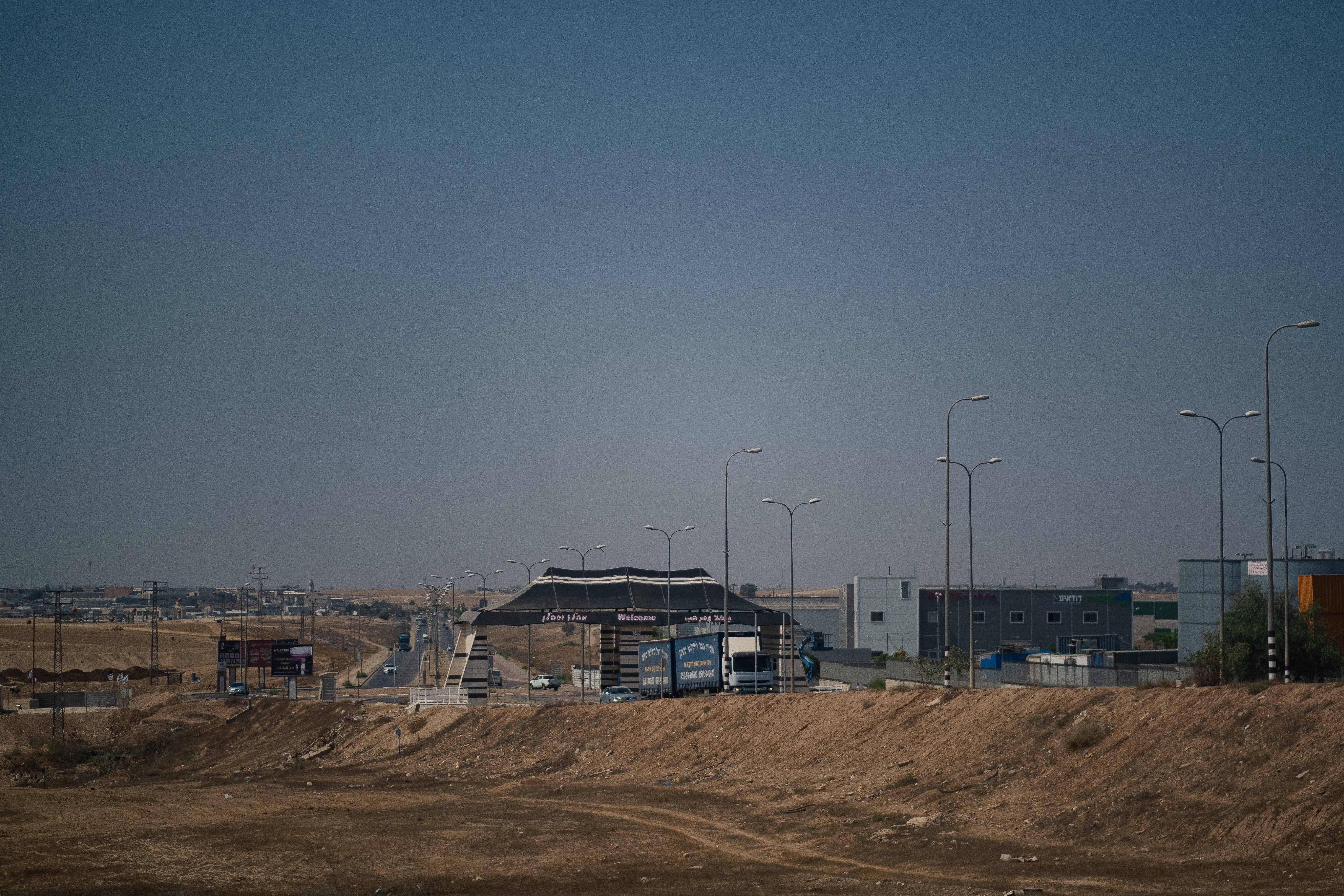 Israel 桌布 壁紙 — 一個廣角鏡頭拍攝的塵土飛揚的城市景觀，一座大型建築和卡車在朦朧的藍天下。
