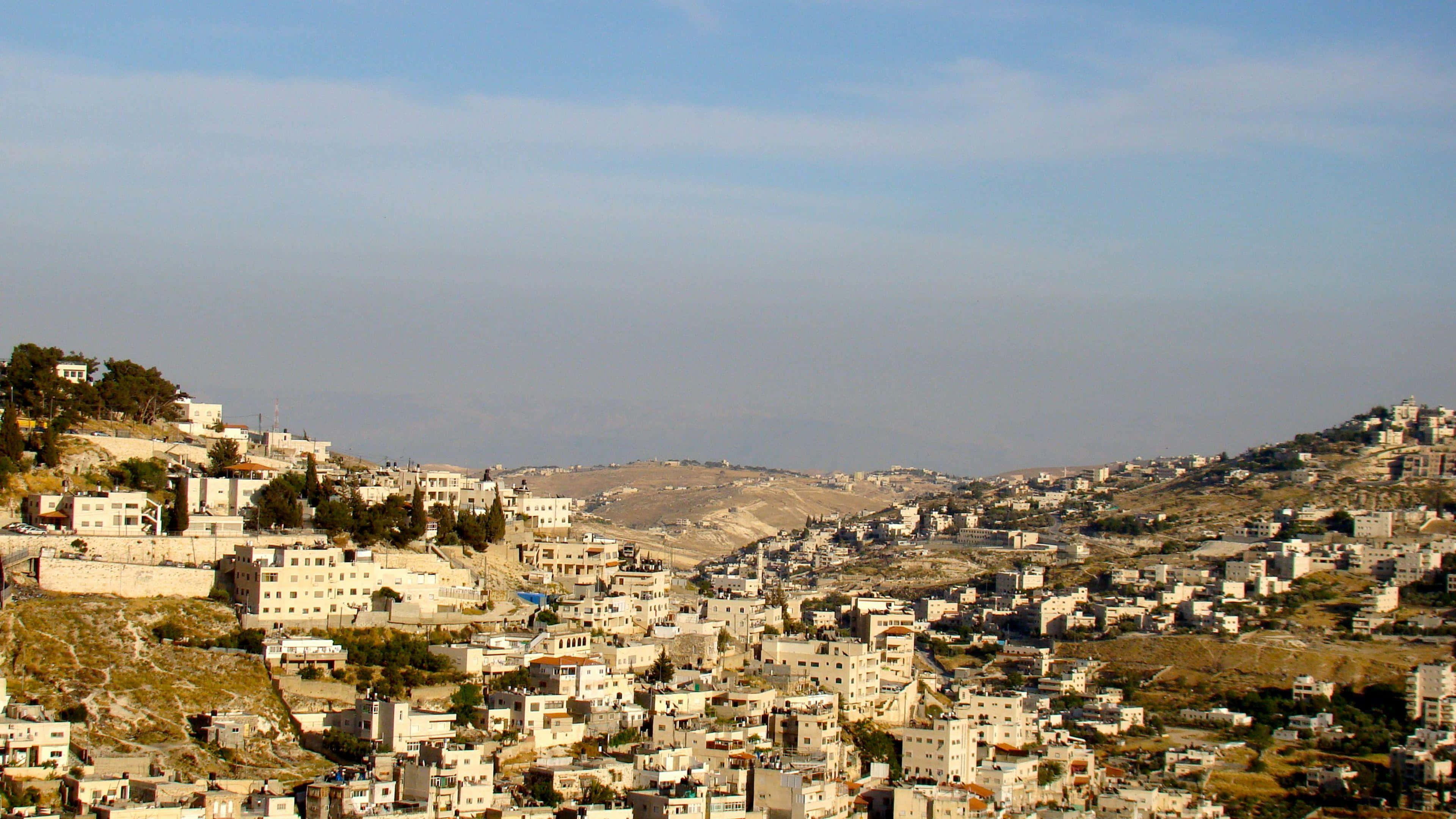 Israel 桌布 壁紙 — 一個廣闊的山坡小鎮，白色建築物坐落在乾燥的山丘之間，天空朦朧湛藍。