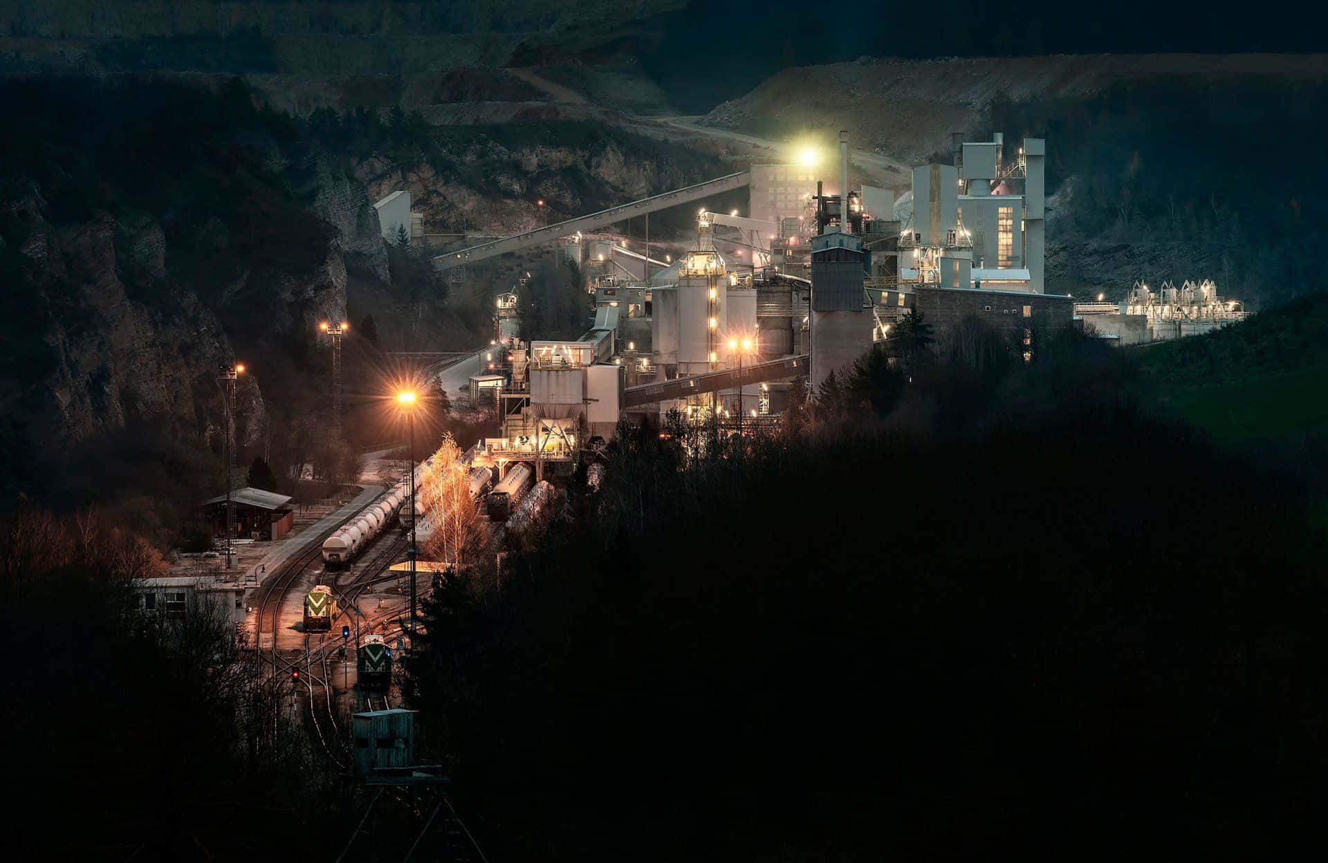Mining 桌布 壁紙 — 一個廣闊的工業園區在夜間以人造燈光映照著黑暗的森林山坡。