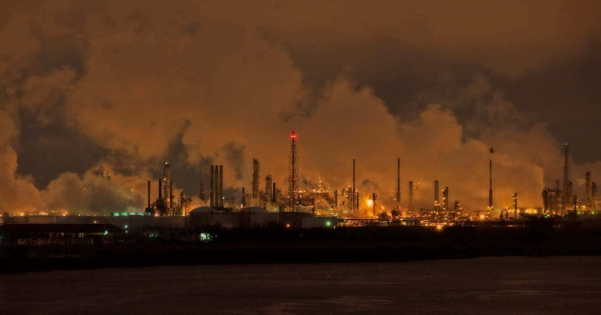 Industry 桌布 壁紙 — 一個廣闊的工業園區在煙霧瀰漫的夜空下發出橙色光芒，倒映在漆黑的水面上。