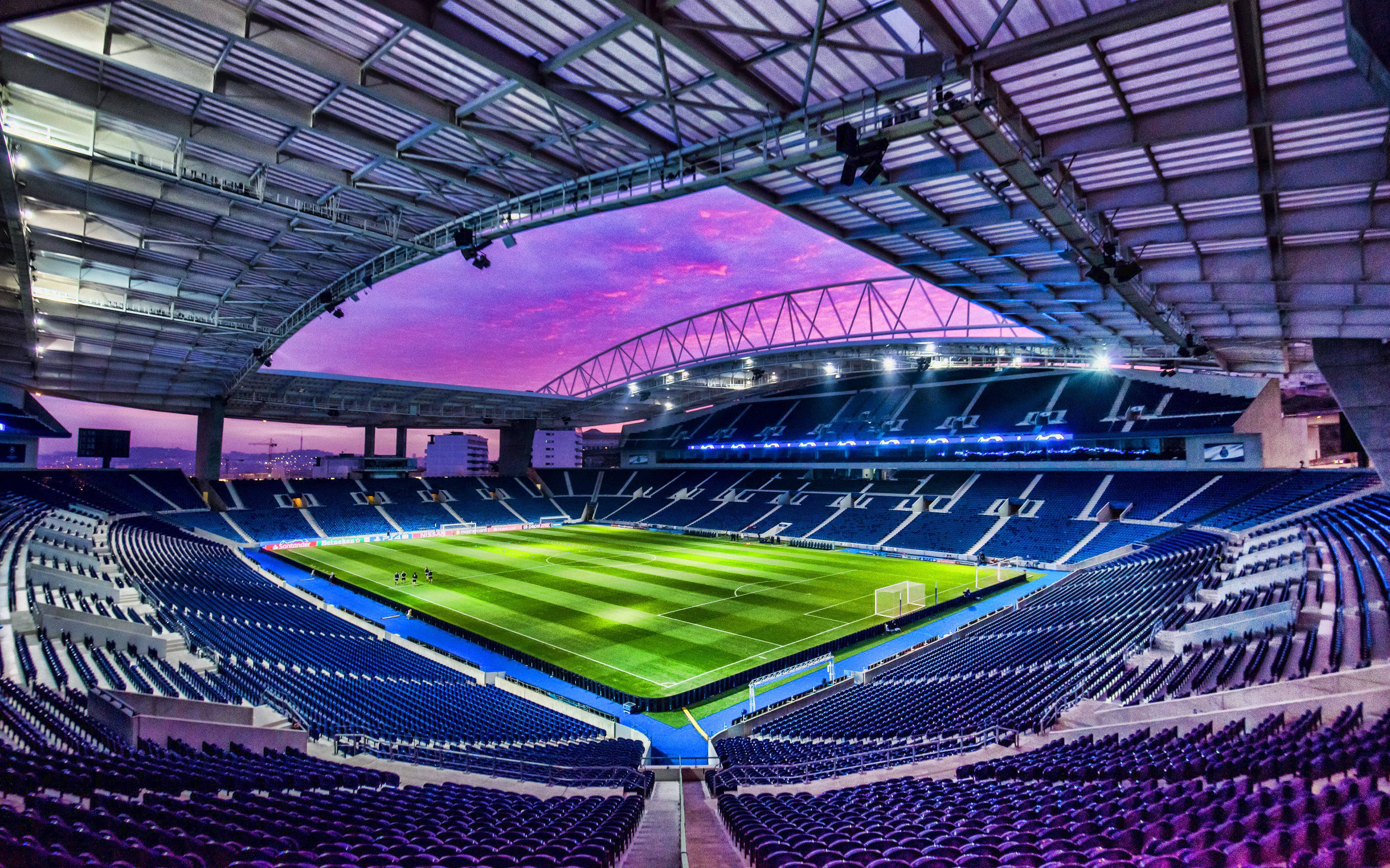 Stadium 桌布 壁紙 — 一個廣闊的空蕩蕩的足球場在黃昏時分，有充滿活力的紫色天空和發光的綠色球場，在鋼屋頂下。