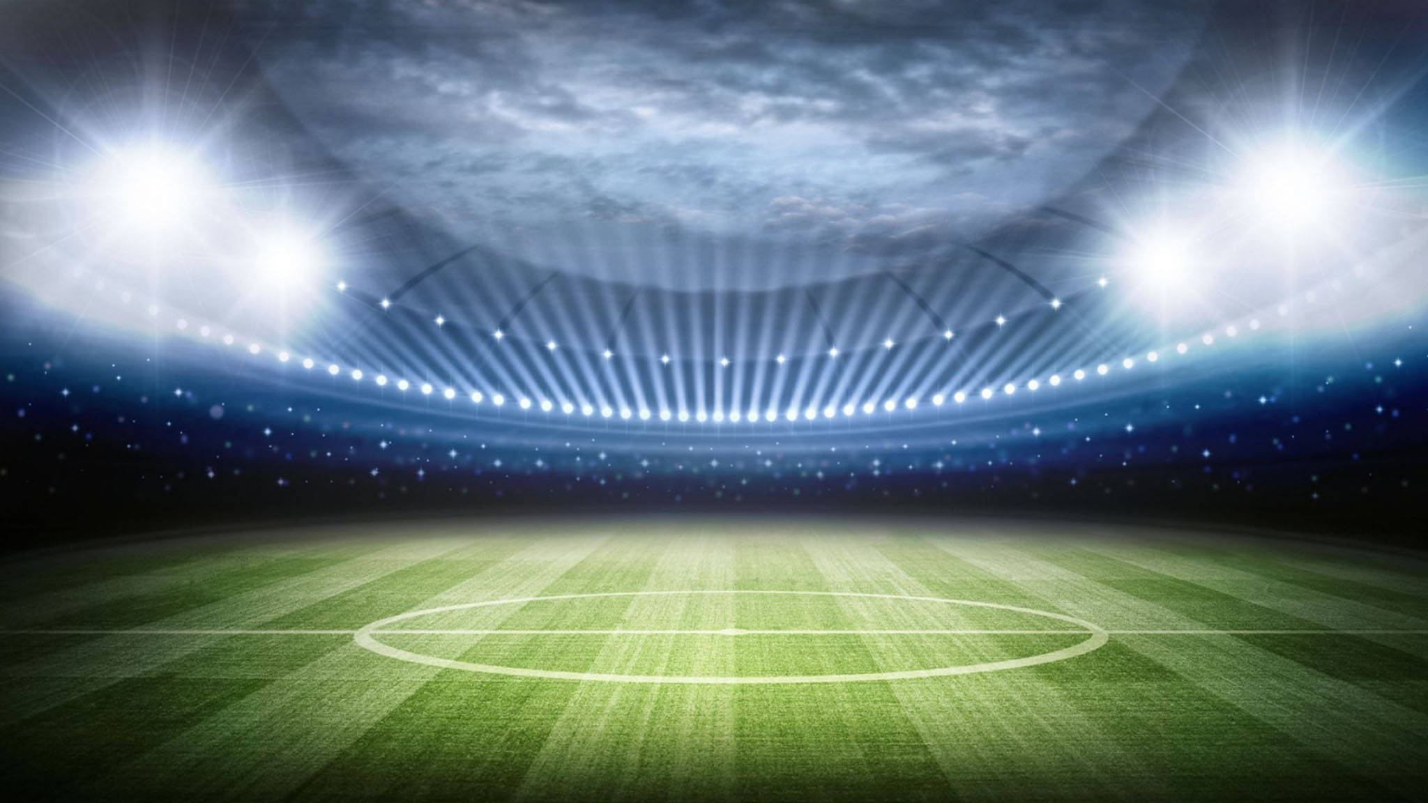 Stadium 桌布 壁紙 — 一個廣闊的空蕩蕩足球場，在戲劇性的夜燈下，有鮮綠色的草地和上方旋轉的雲層。