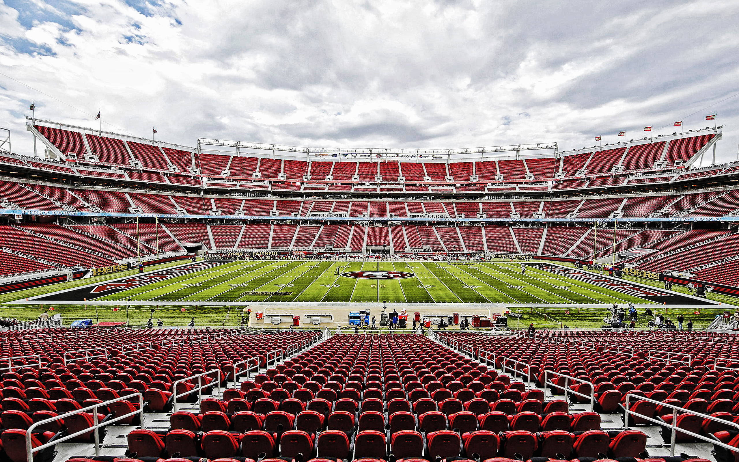 Stadium 桌布 壁紙 — 一個廣闊空曠的足球場，紅色座位和綠色球場，天空多雲。