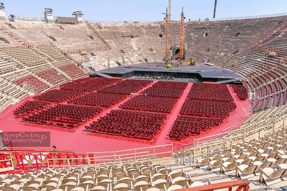 Roman Colosseum 桌布 壁紙 — 一個廣闊空曠的體育館，紅色座位排列成蜿蜒的排，在晴朗的藍天下可見建築起重機。