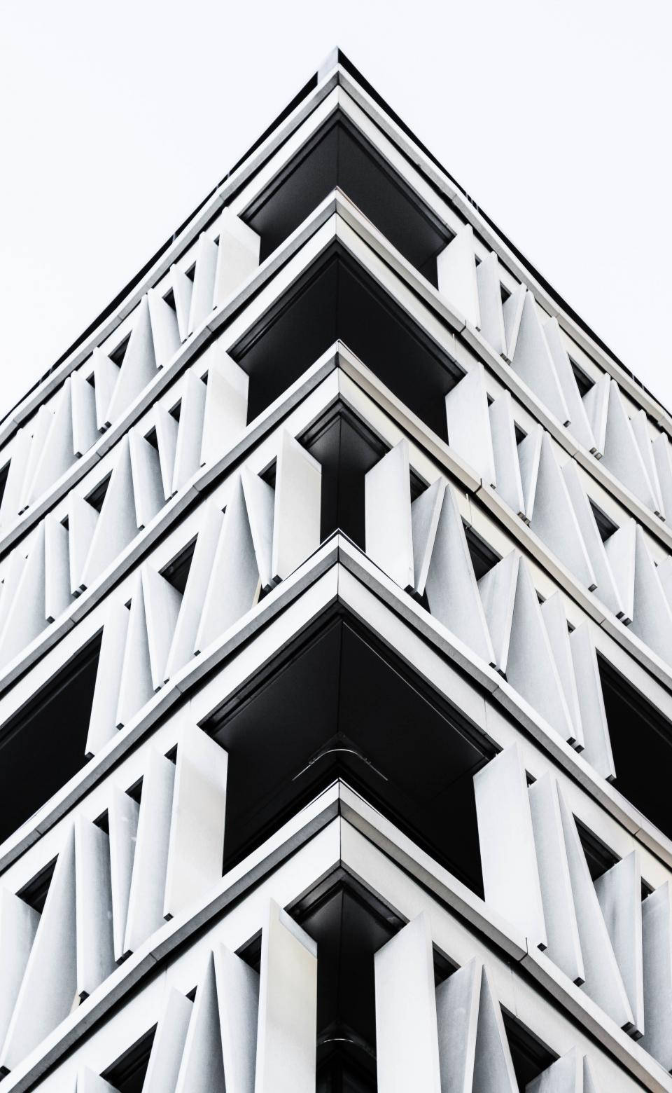 Architecture 桌布 壁紙 — 一個引人注目的低角度視角，展現現代建築角落，帶有鮮明的白色幾何圖案和深黑色凹陷，襯托著蒼白的天空。