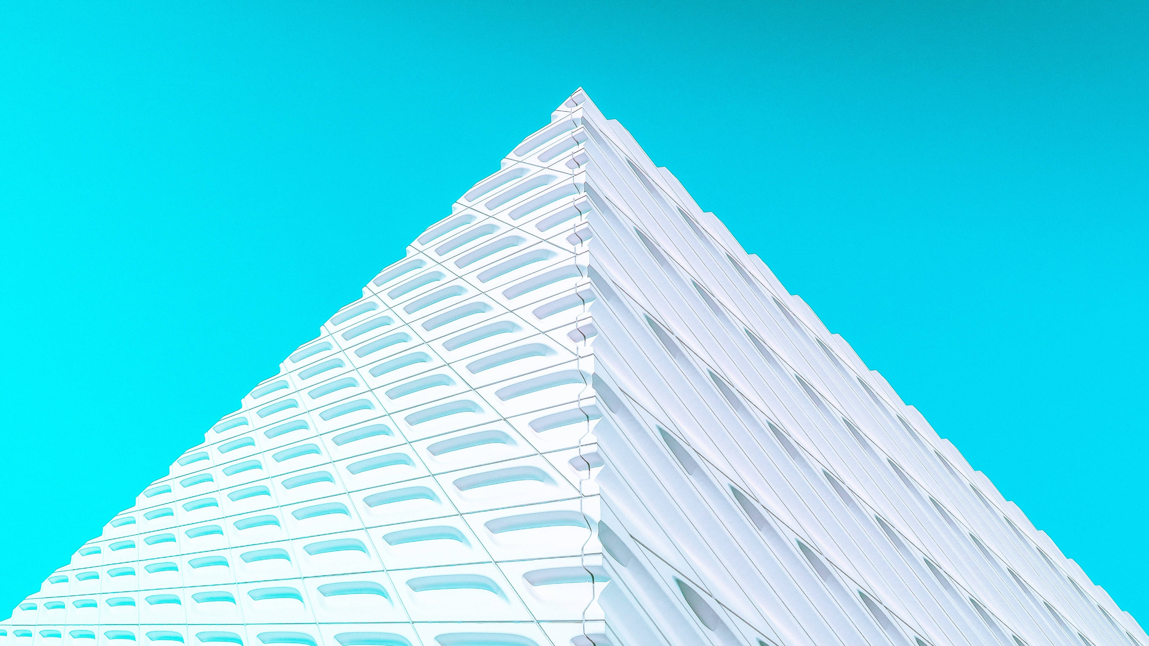 Building 桌布 壁紙 — 一個引人注目的低角度視角，白色幾何金字塔形建築物襯著鮮豔的青色天空。