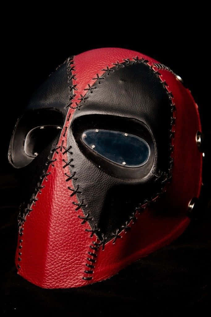 Deadpool Mask 桌布 壁紙 — 一個引人注目的紅黑皮革面具，帶有十字繡細節和藍色眼罩，背景為深色。