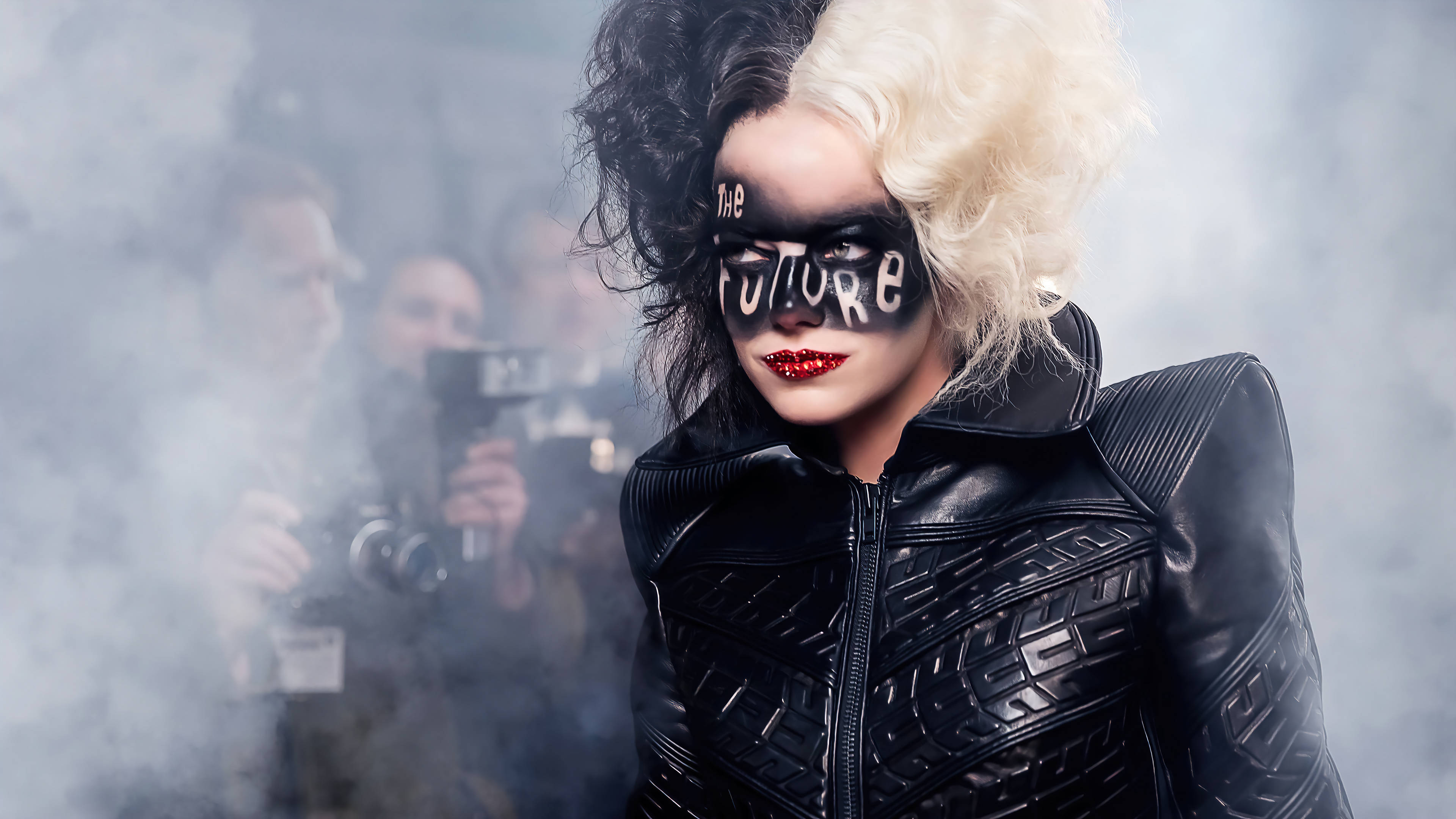 Cruella 桌布 壁紙 — 一個引人注目的角色，頭髮半黑半金，眼睛上畫著「The Future」，透過煙霧迷濛的薄霧凝視著。