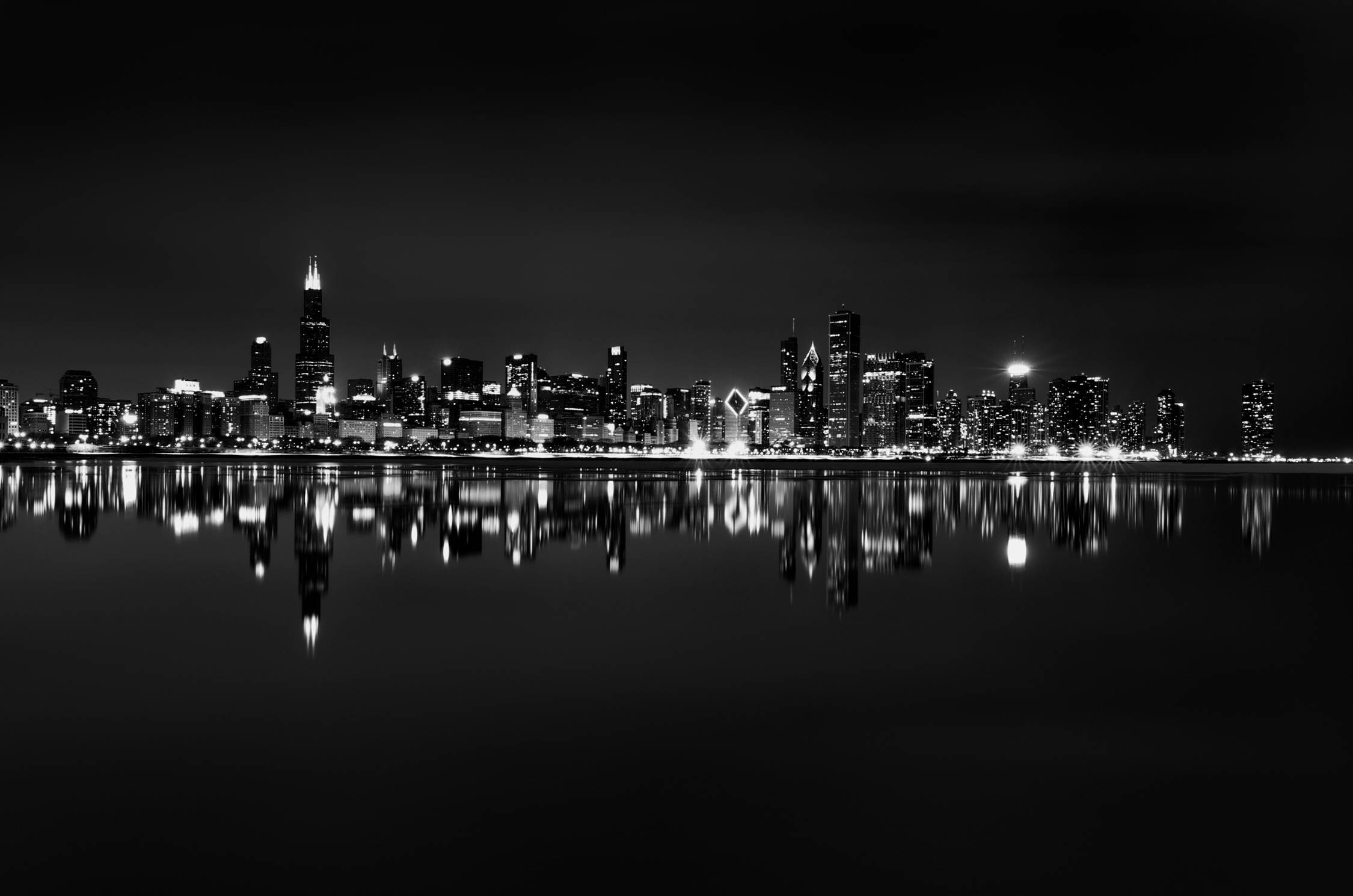 城市 桌布 壁紙 — 一個引人注目的黑白城市夜景，摩天大樓完美倒映在平靜的水面上。