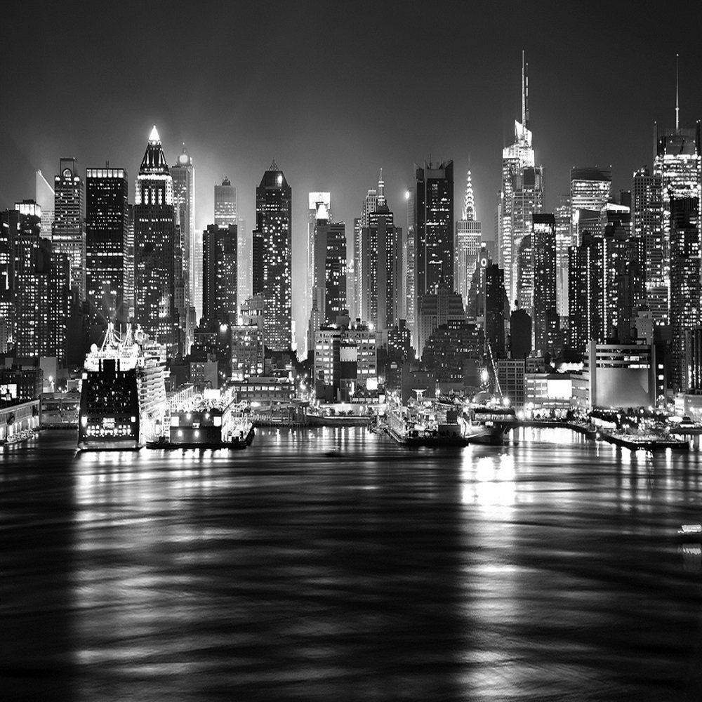 New York 桌布 壁紙 — 一個引人注目的黑白夜景，密集的城市天際線，明亮的摩天大樓倒映在平靜的水面上。