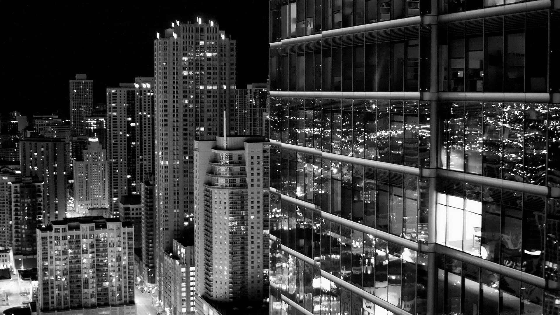 Buildings 桌布 壁紙 — 一個引人注目的黑白夜景城市景觀，高聳的摩天大樓在其玻璃外牆上反射出閃爍的光芒。