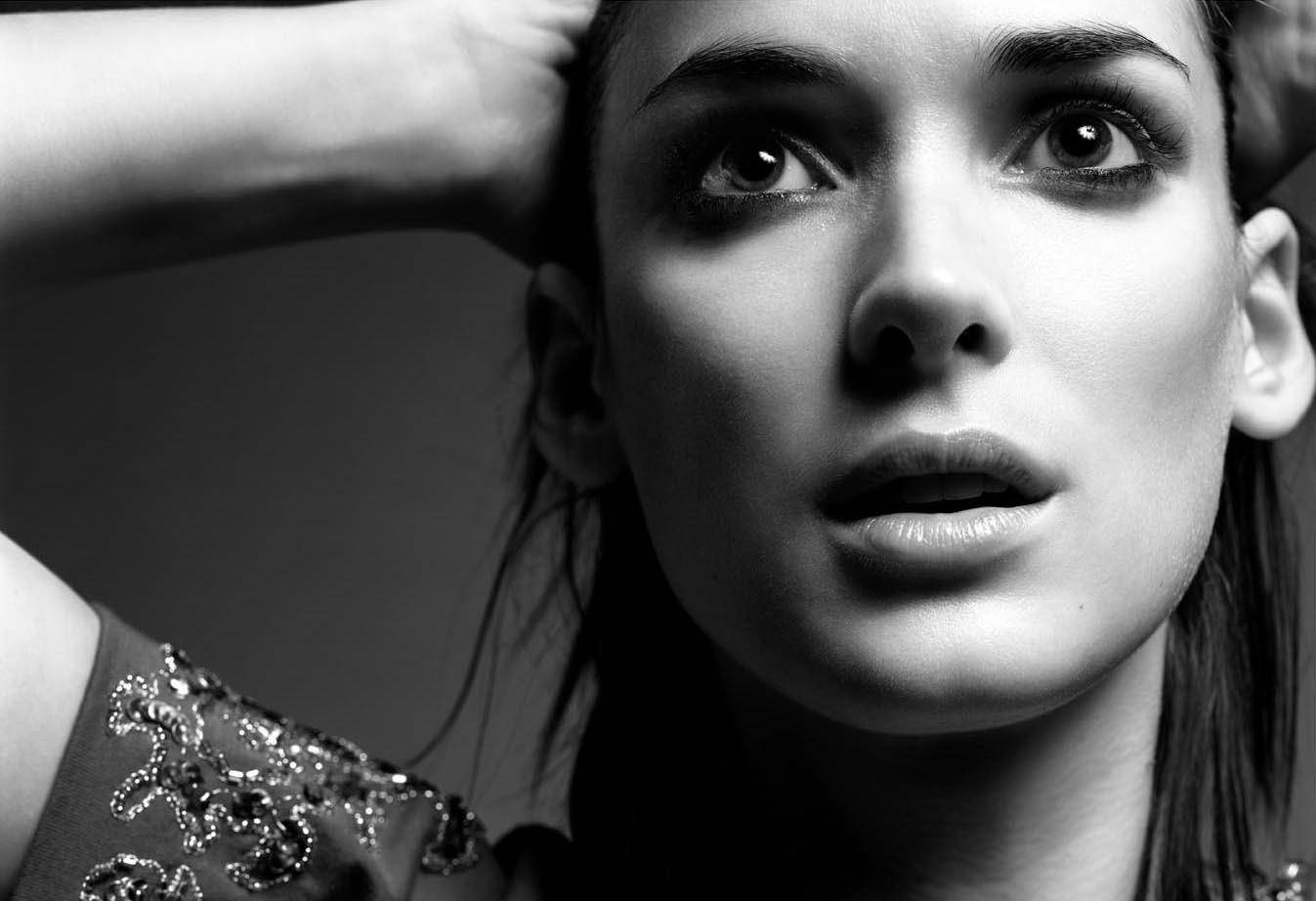 winona ryder 桌布 壁紙 — 一個引人注目的黑白特寫，一位眼神強烈、手放在頭髮中的女性，穿著珠飾上衣。