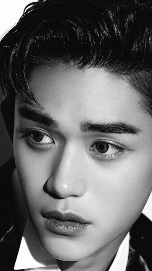 K-pop 桌布 壁紙 — 一個引人注目的黑白特寫肖像，描繪一位眼神銳利、髮型時尚的年輕男子。