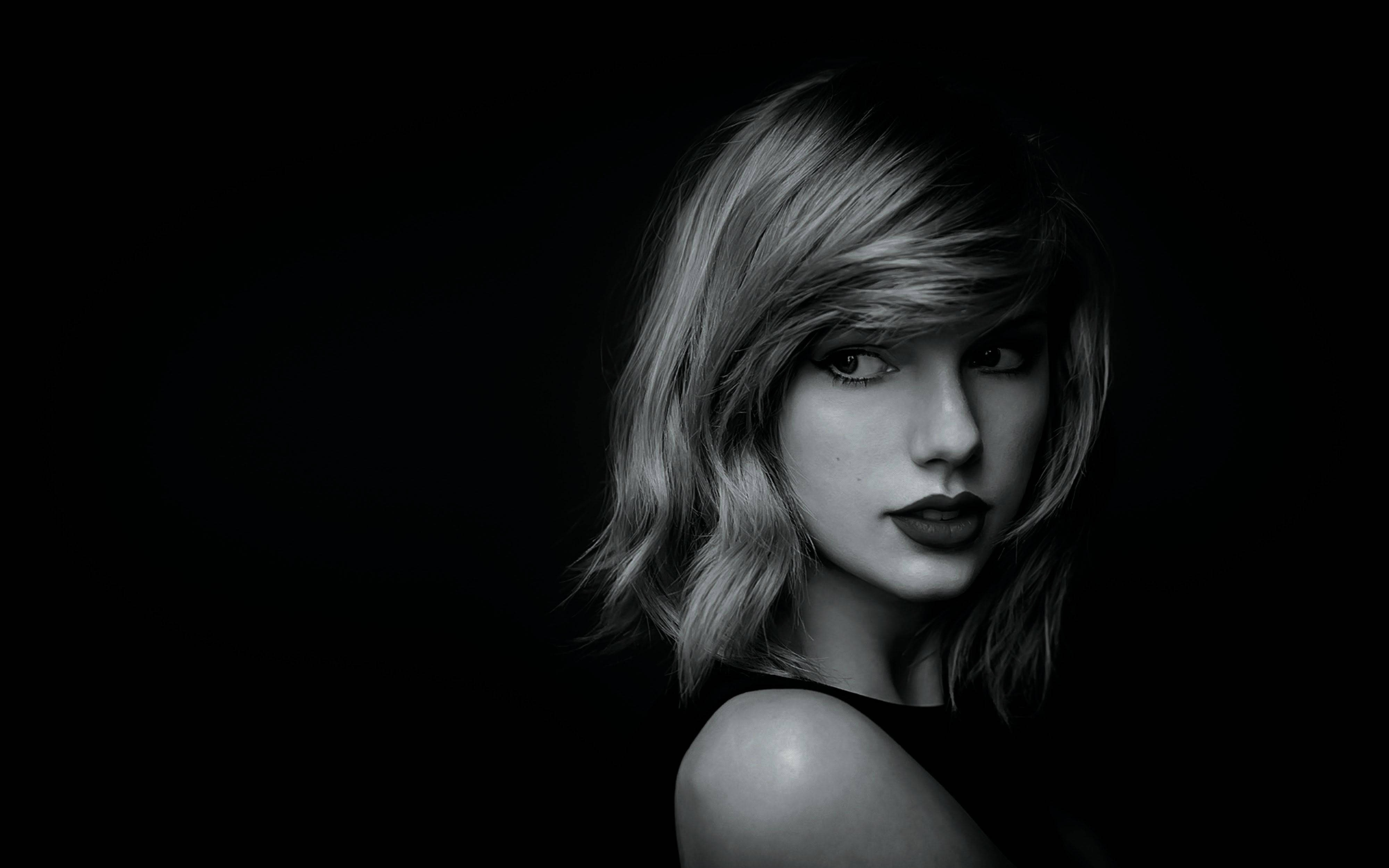 Taylor Swift 桌布 壁紙 — 一個引人注目的黑白肖像，一位女性擁有柔軟的波浪和鮮明的嘴唇，背景是深黑色。