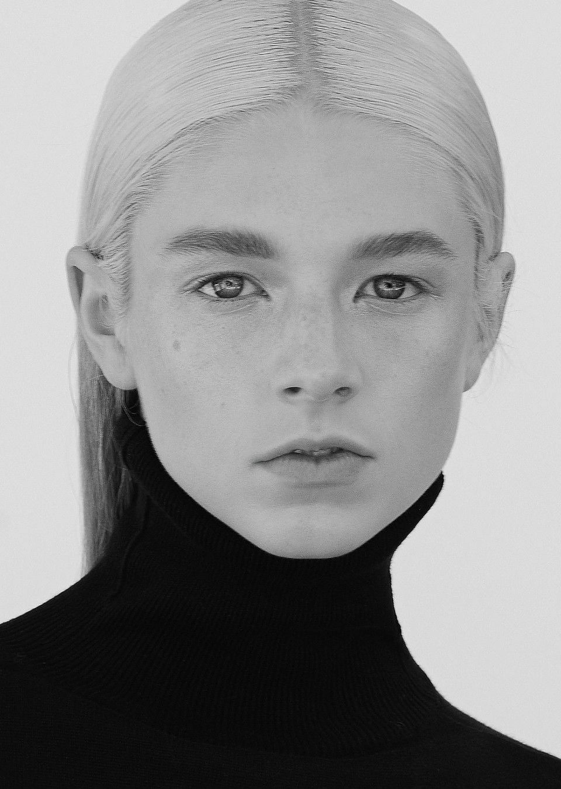 Hunter Schafer 桌布 壁紙 — 一個引人注目的黑白肖像，一位年輕女性擁有鉑金色頭髮和雀斑，穿著高領 turtleneck。