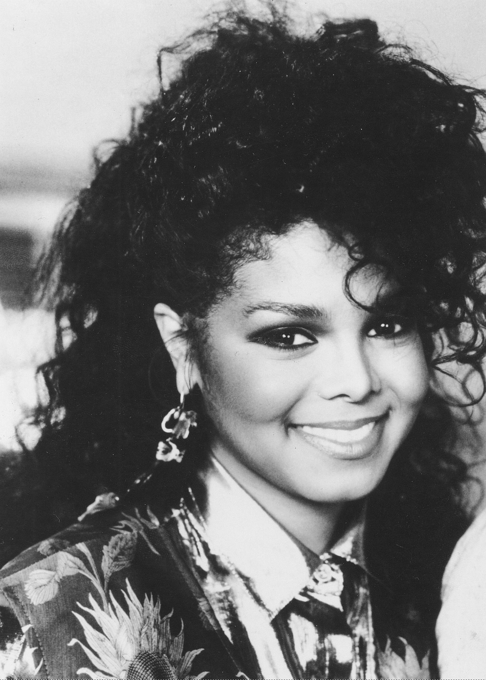 janet jackson 桌布 壁紙 — 一個引人注目的黑白肖像，一位擁有豐盈捲髮的女性對著鏡頭溫暖微笑。