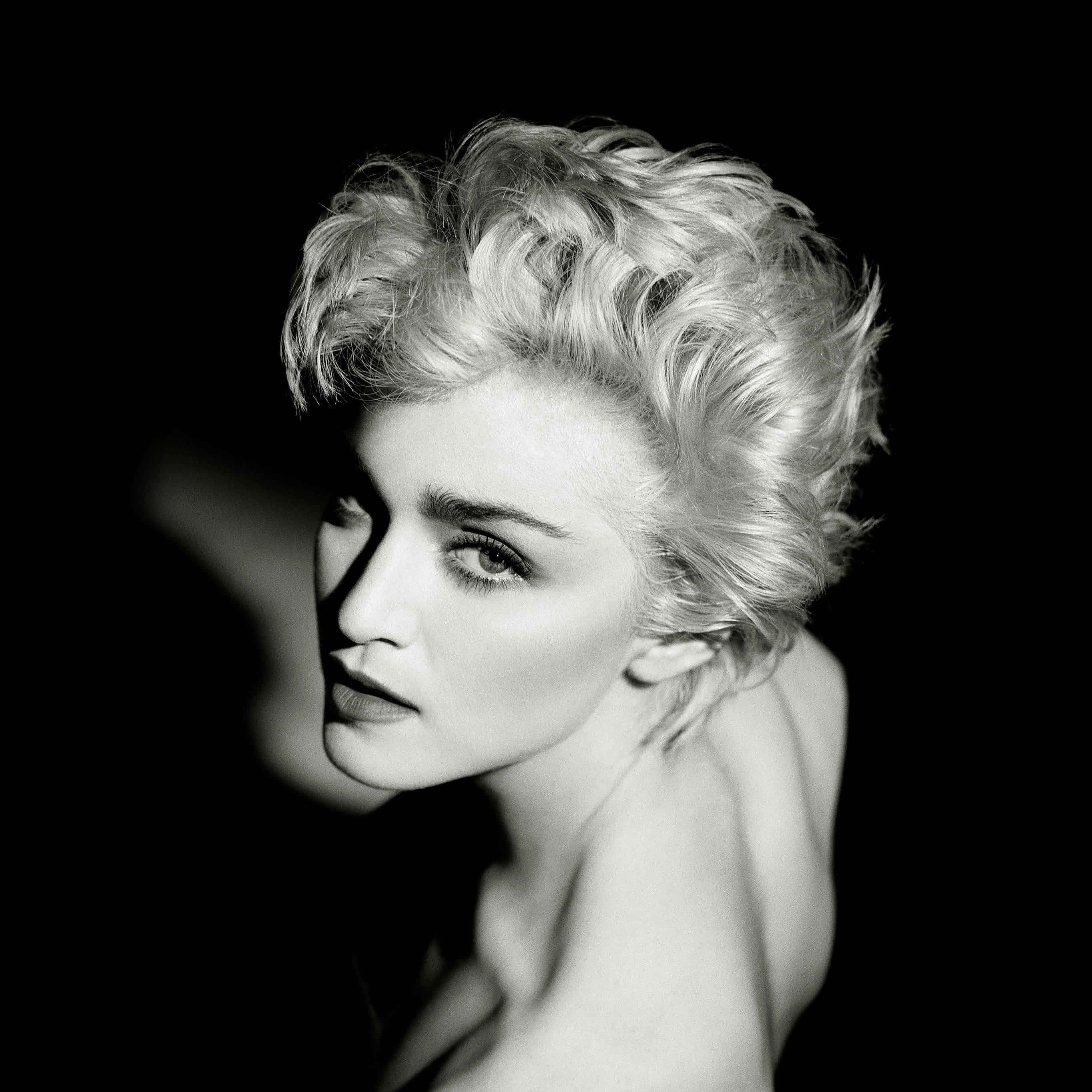 Madonna 桌布 壁紙 — 一個引人注目的黑白肖像，一位擁有豐盈金髮的女性在黑暗背景下凝視著。