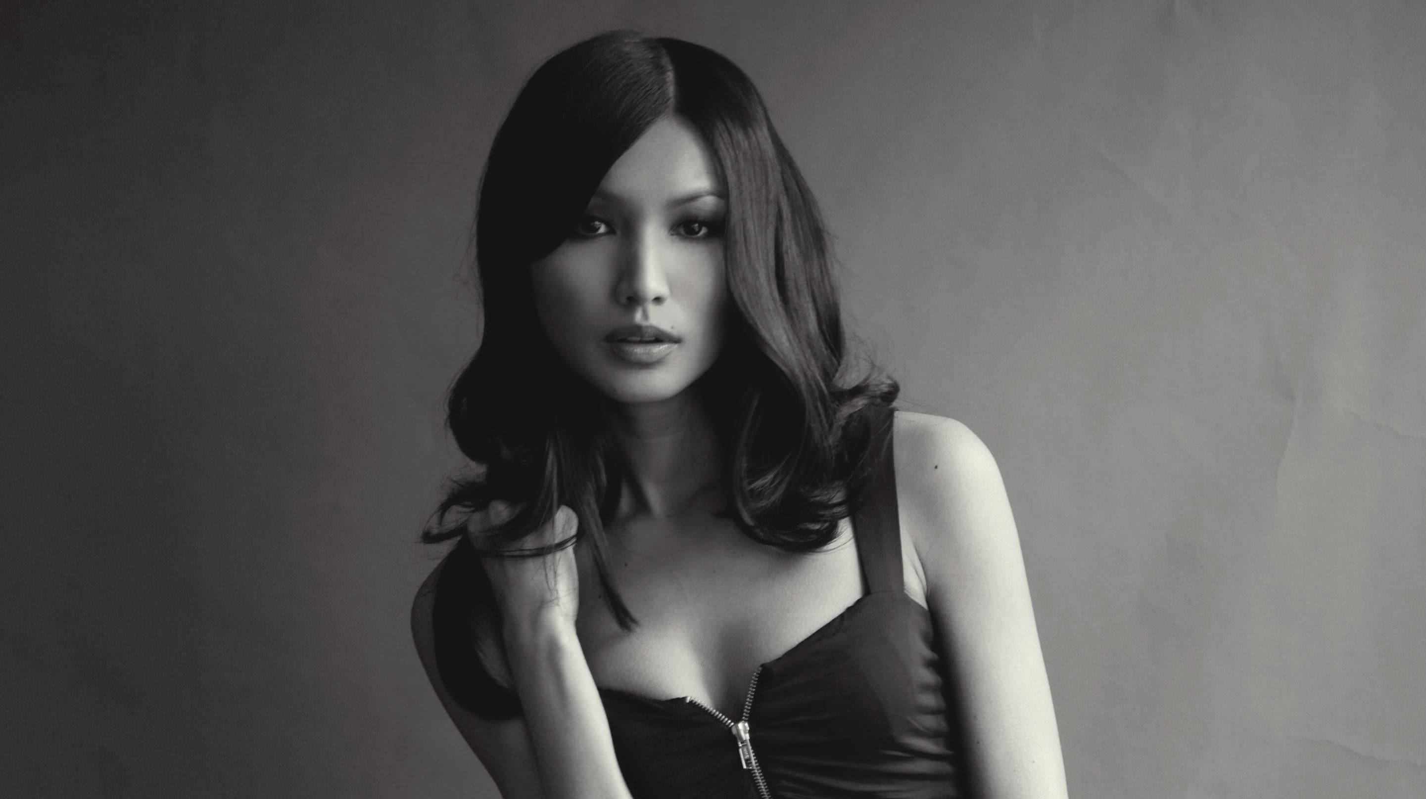 Gemma Chan 桌布 壁紙 — 一個引人注目的黑白肖像，一位波浪髮型的女性在純灰色背景下直視鏡頭。