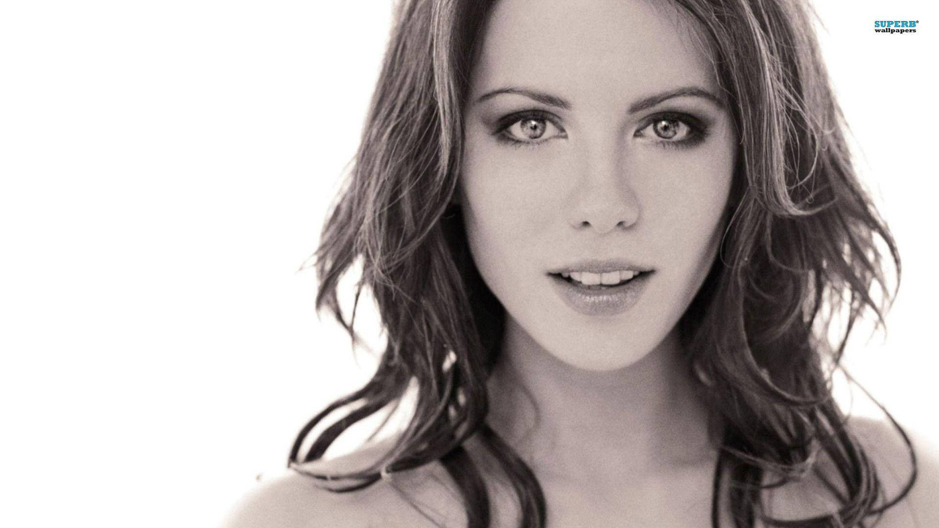 Kate Beckinsale 桌布 壁紙 — 一個引人注目的黑白肖像，一位波浪頭髮的女性在明亮的白色背景下直視鏡頭。