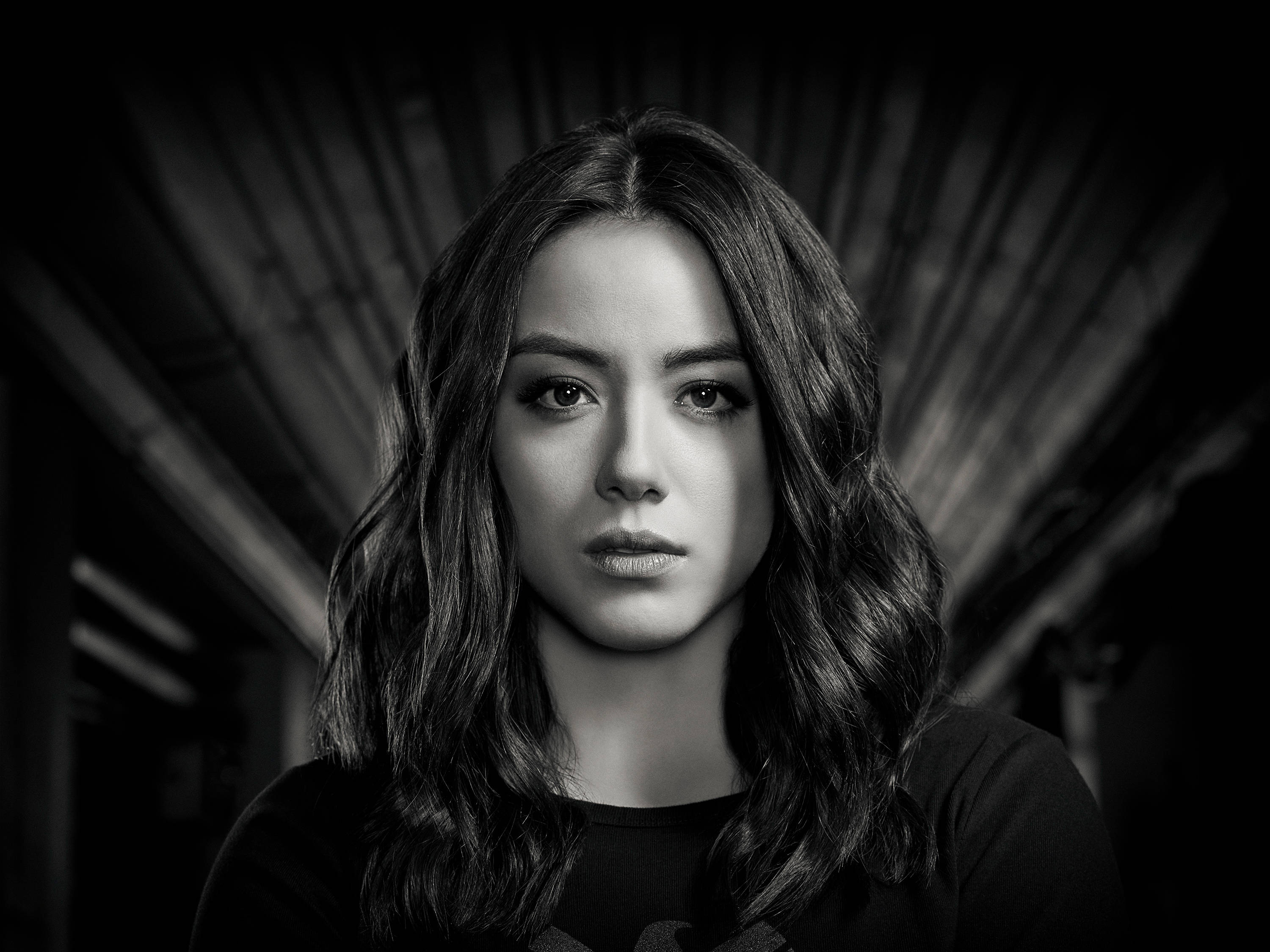chloe bennet 桌布 壁紙 — 一個引人注目的黑白肖像，一位波浪長髮的女性在深色紋理背景前，強烈地凝視著鏡頭。