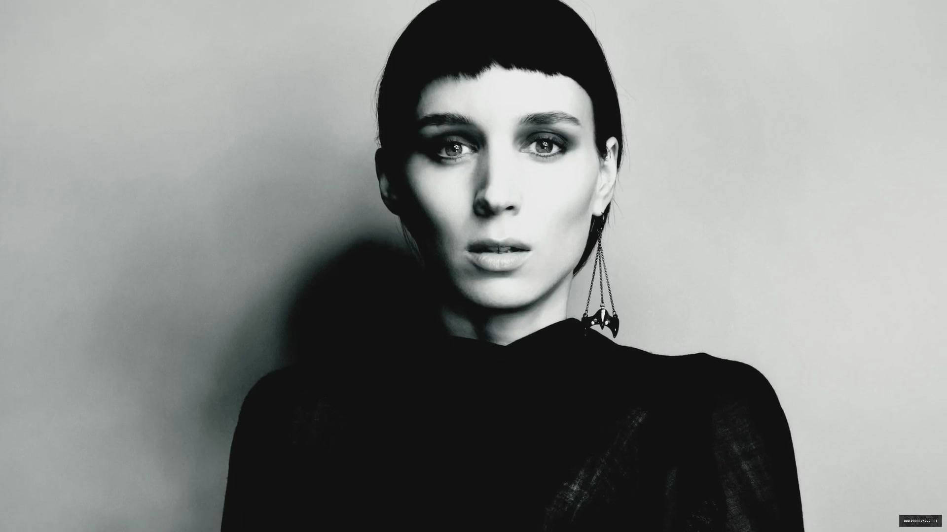 Rooney Mara 桌布 壁紙 — 一個引人注目的黑白肖像，一位短黑髮、戴著大膽耳環的女性，強烈地凝視著鏡頭。