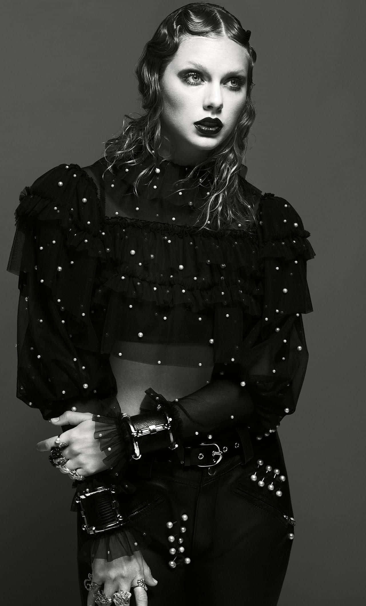 Taylor Swift iPhone 桌布 壁紙 — 一個引人注目的黑白肖像，一位穿著珍珠裝飾哥德式服裝的女性在純灰色背景前擺姿勢。