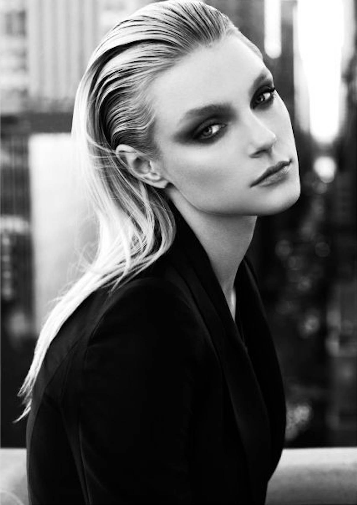 jessica stam 桌布 壁紙 — 一個引人注目的黑白肖像，一位金髮女性帶有戲劇性的眼妝，在模糊的城市背景下凝視著。